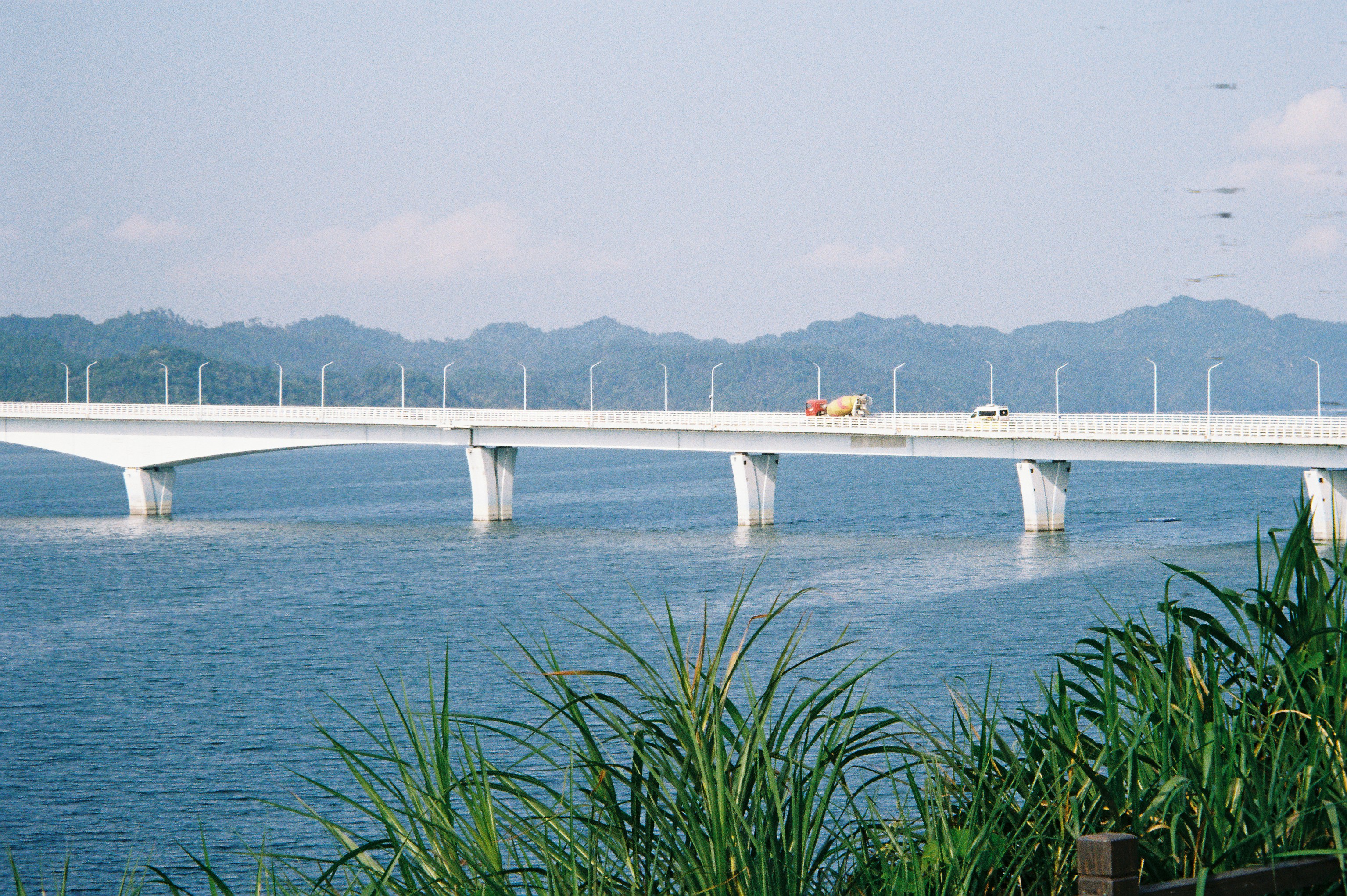 A long white bridge spanning a wide body of water with distant mountains