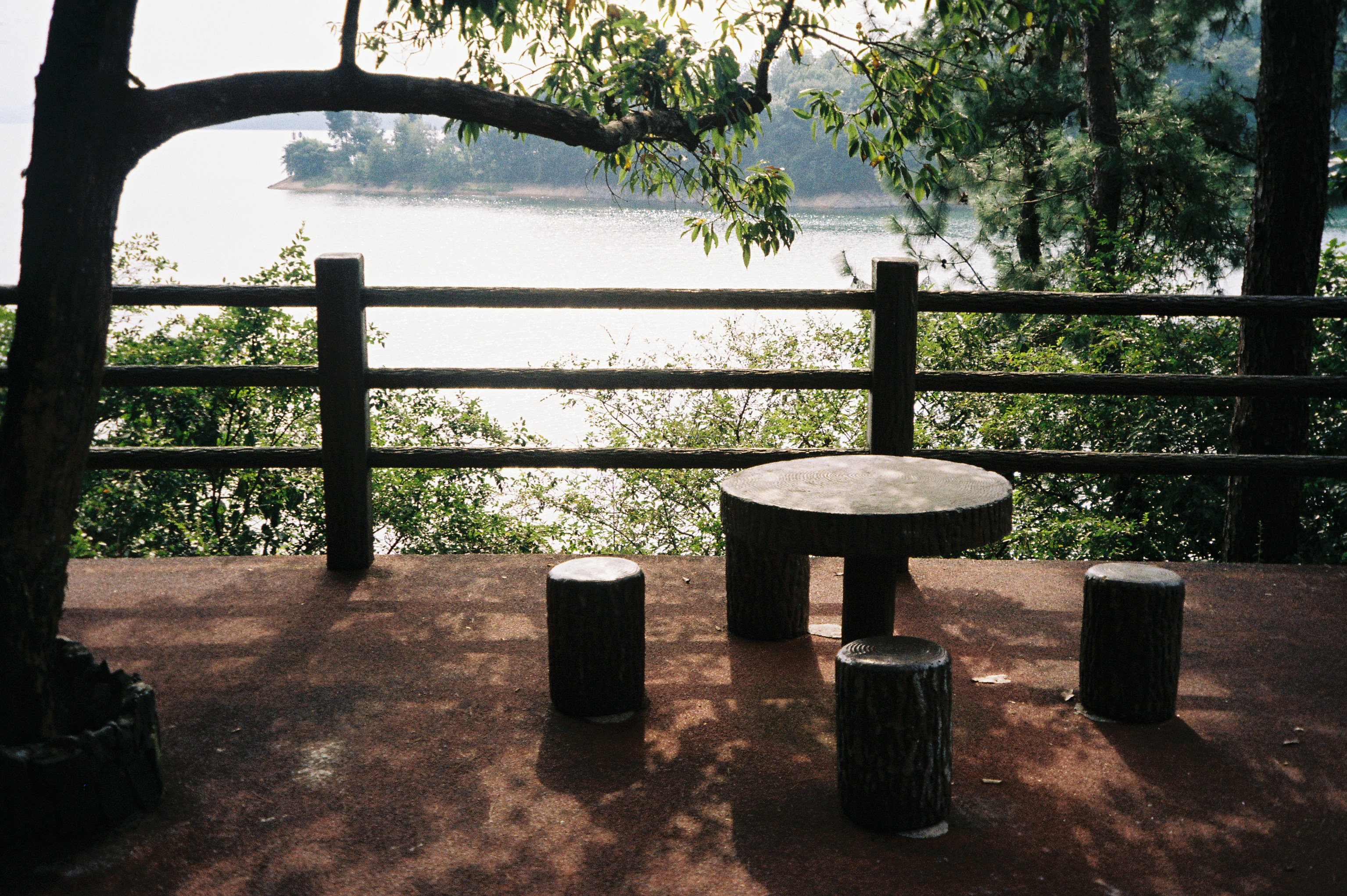 A round table and three stools on a patio overlooking a lake