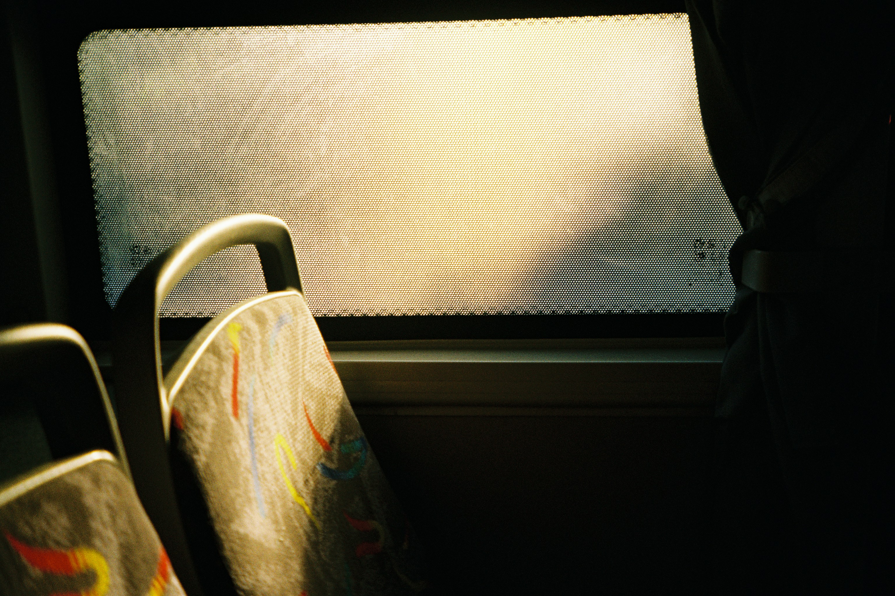 Patterned bus seats in front of a window with a perforated sun shade