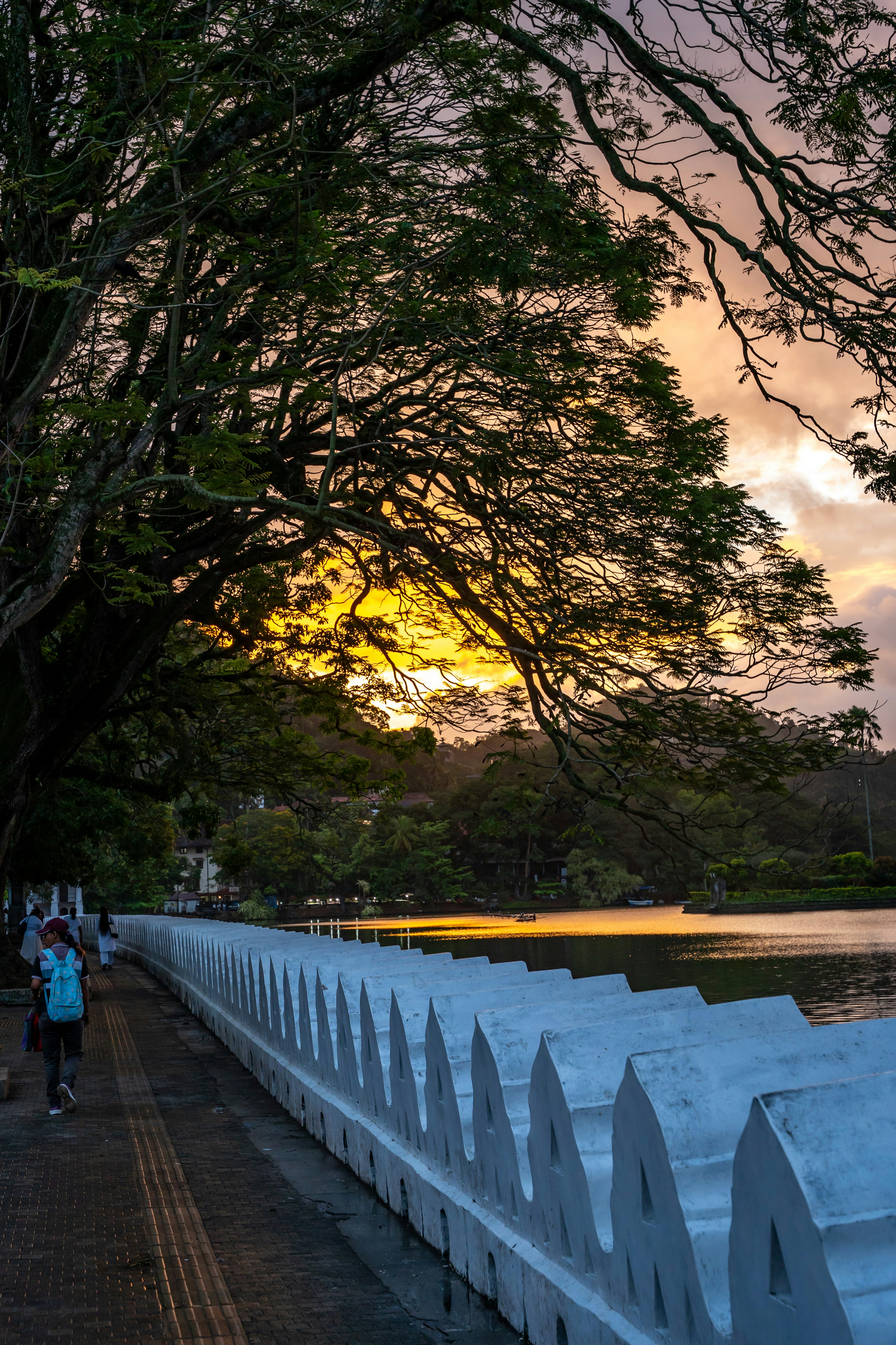 A person with a blue backpack walking along a white wall by a lake