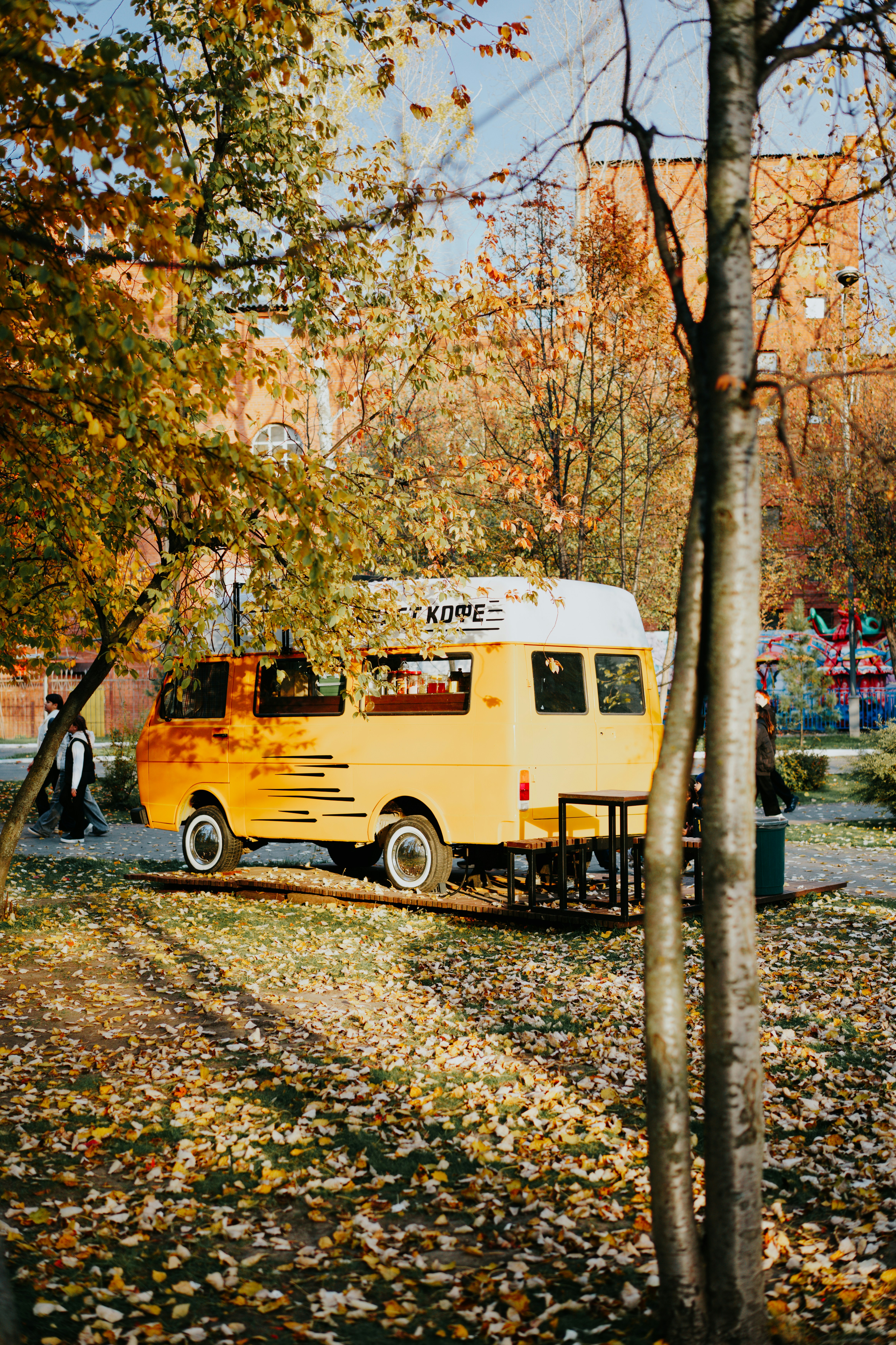 A yellow Kombi food truck parked in a park during autumn