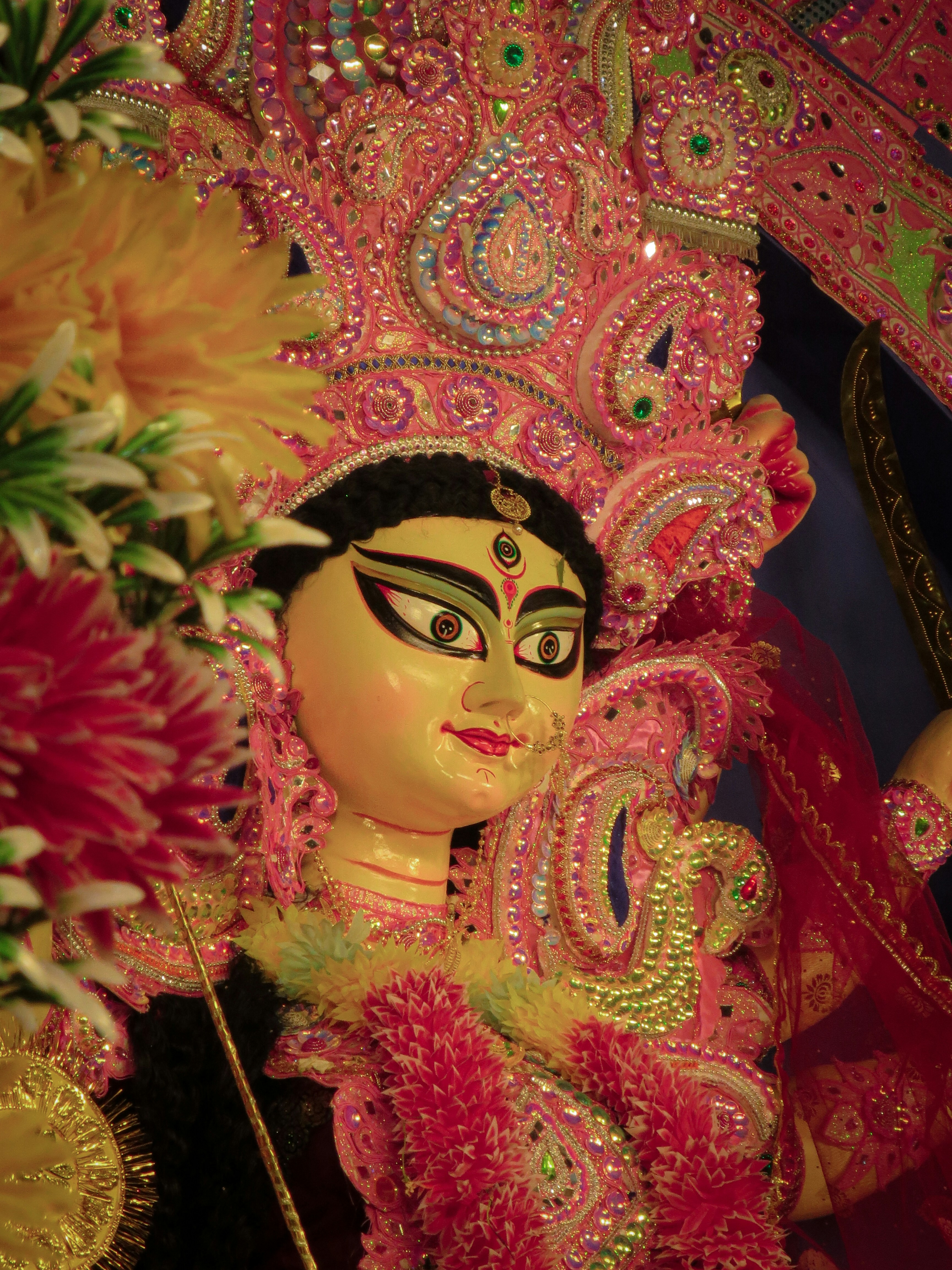 A Durga idol with ornate pink headwear and flowers in the foreground