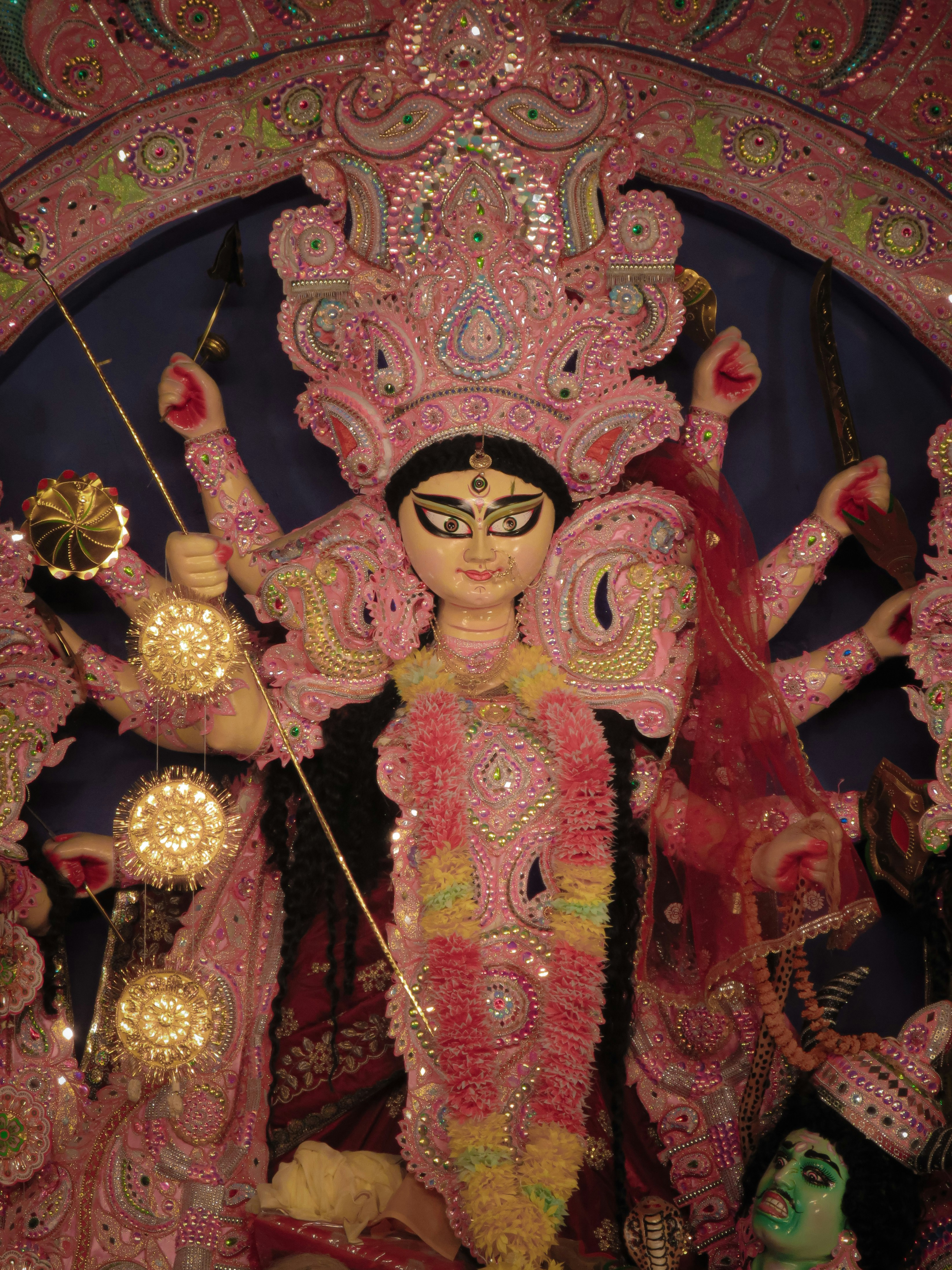 A multi-armed Durga idol adorned with pink and gold ornaments and a red veil