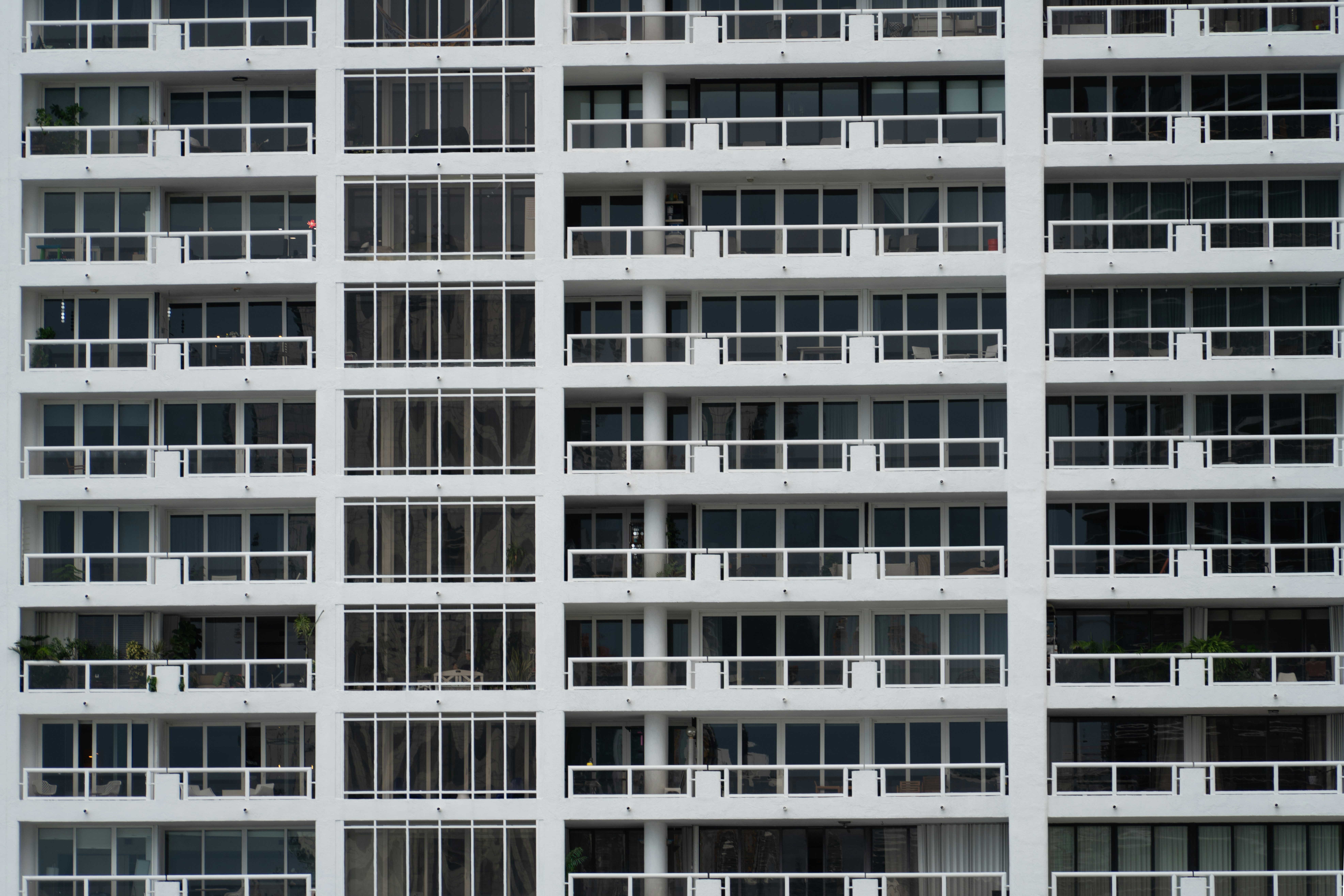 Una fachada blanca de edificio de apartamentos con filas de balcones y puertas correderas de cristal