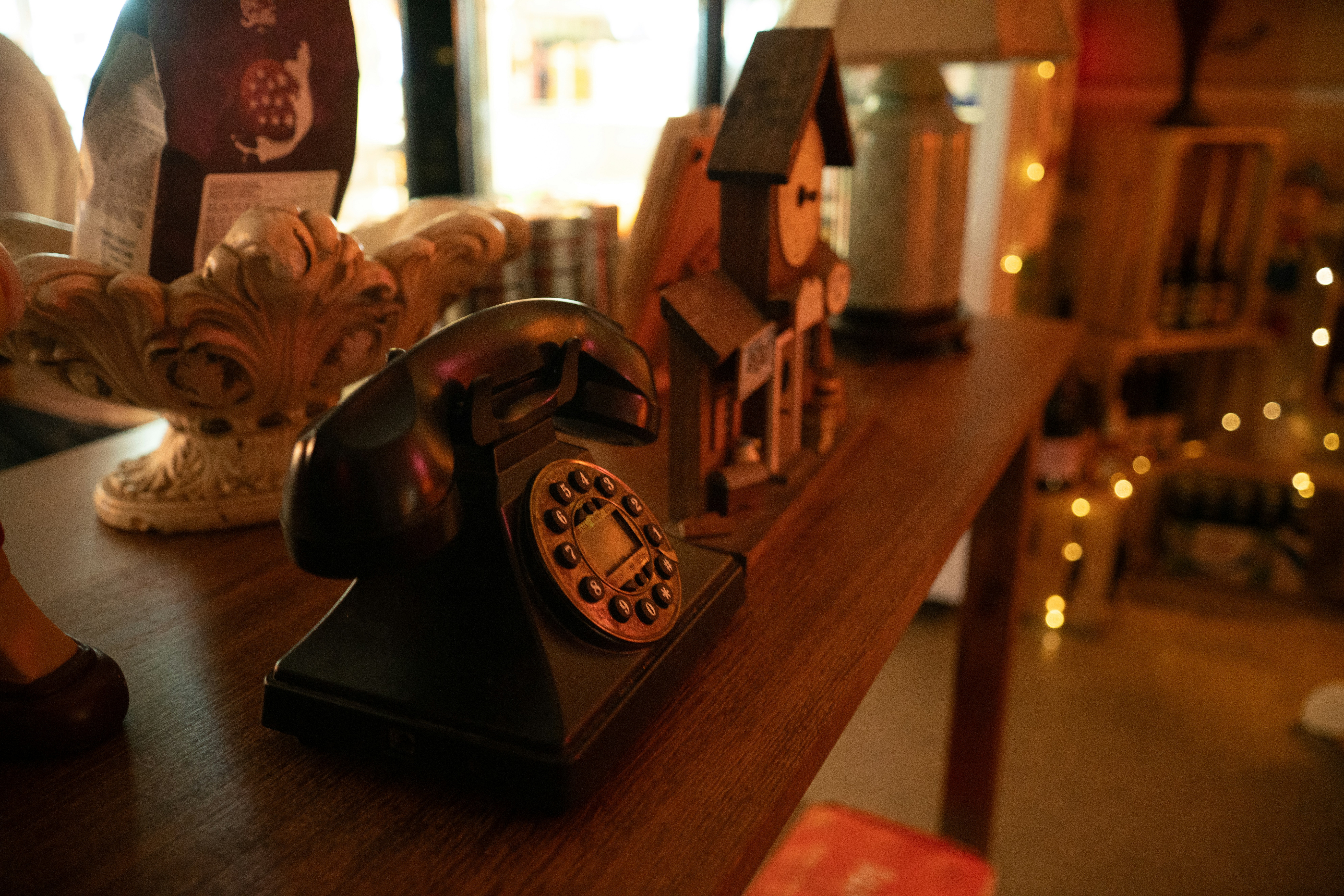 Un teléfono giratorio negro sobre una mesa de madera con un reloj decorativo cerca