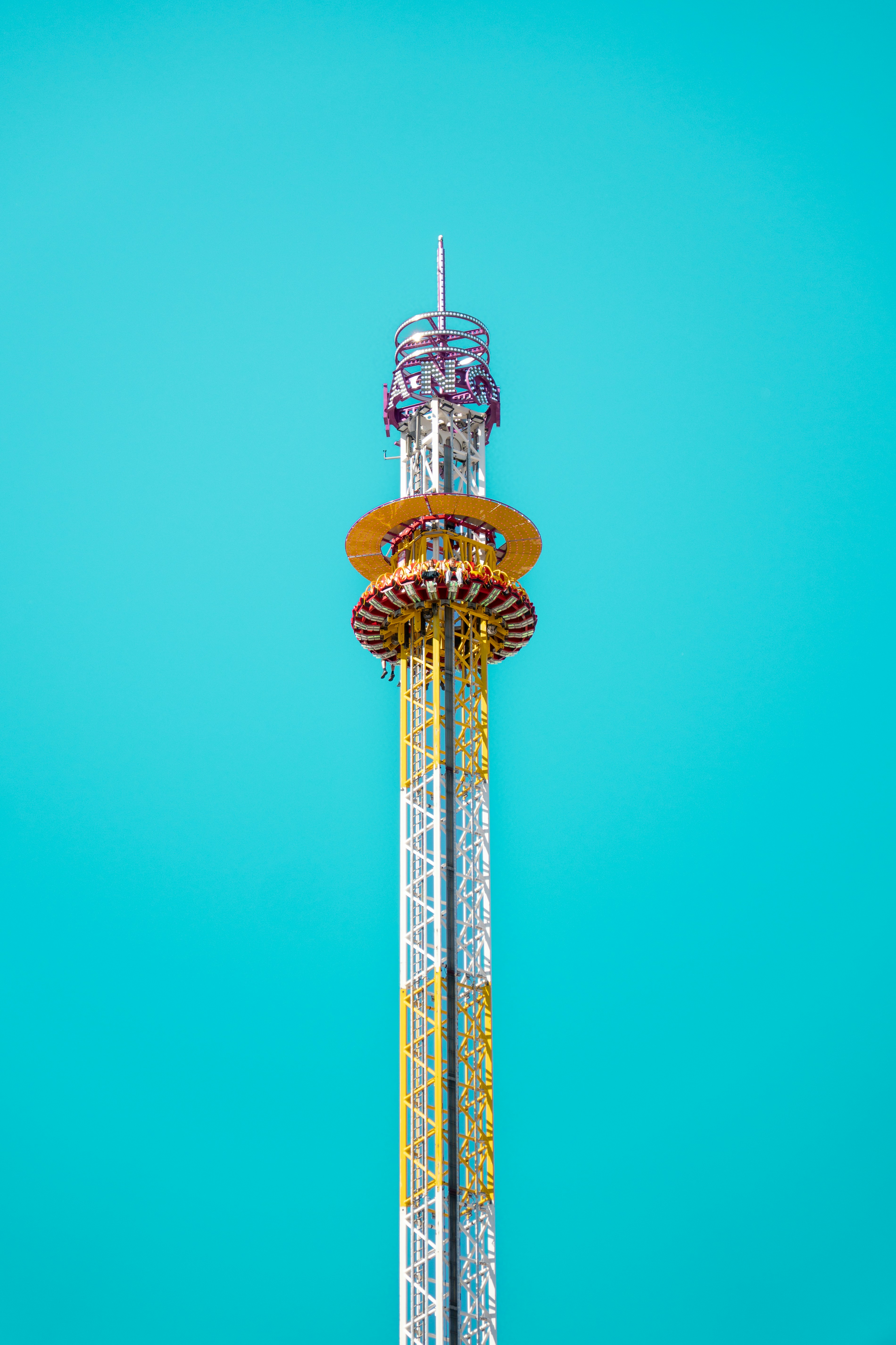 A drop tower amusement ride with a yellow lattice structure against a clear blue sky
