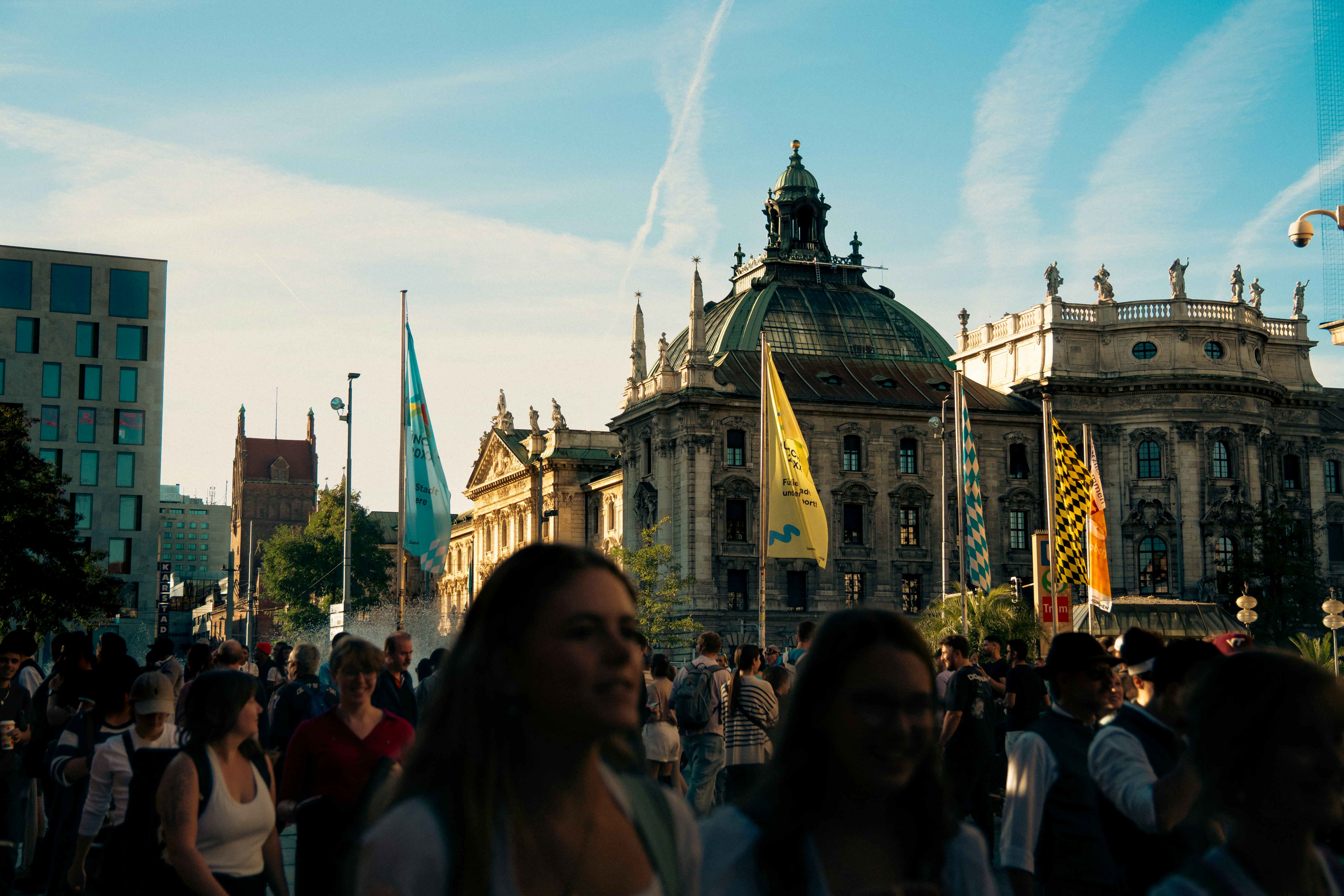 A crowd of people walking across a sunny plaza in front of historic European architecture