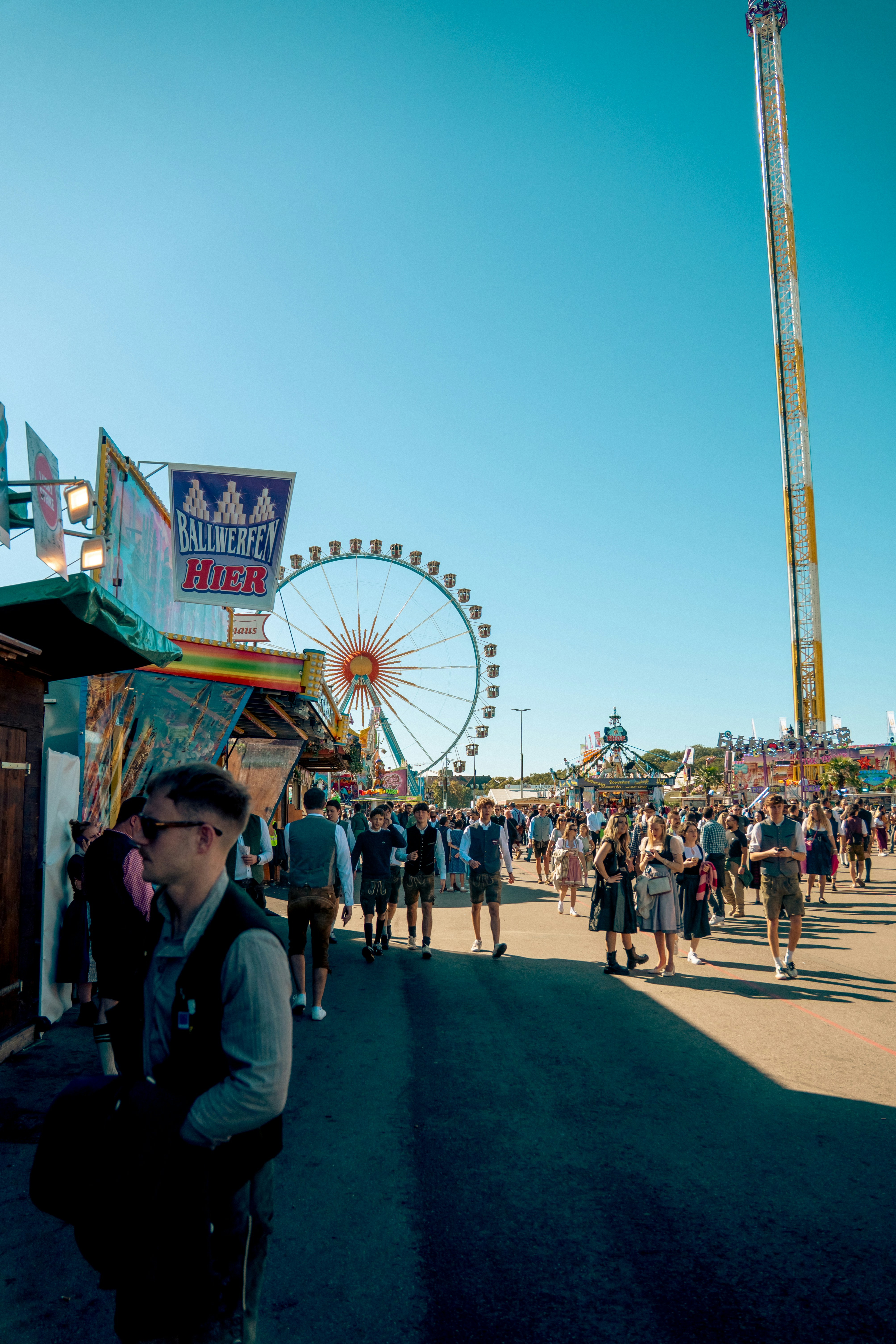 People walking through a fairground with a ferris wheel and tall drop tower