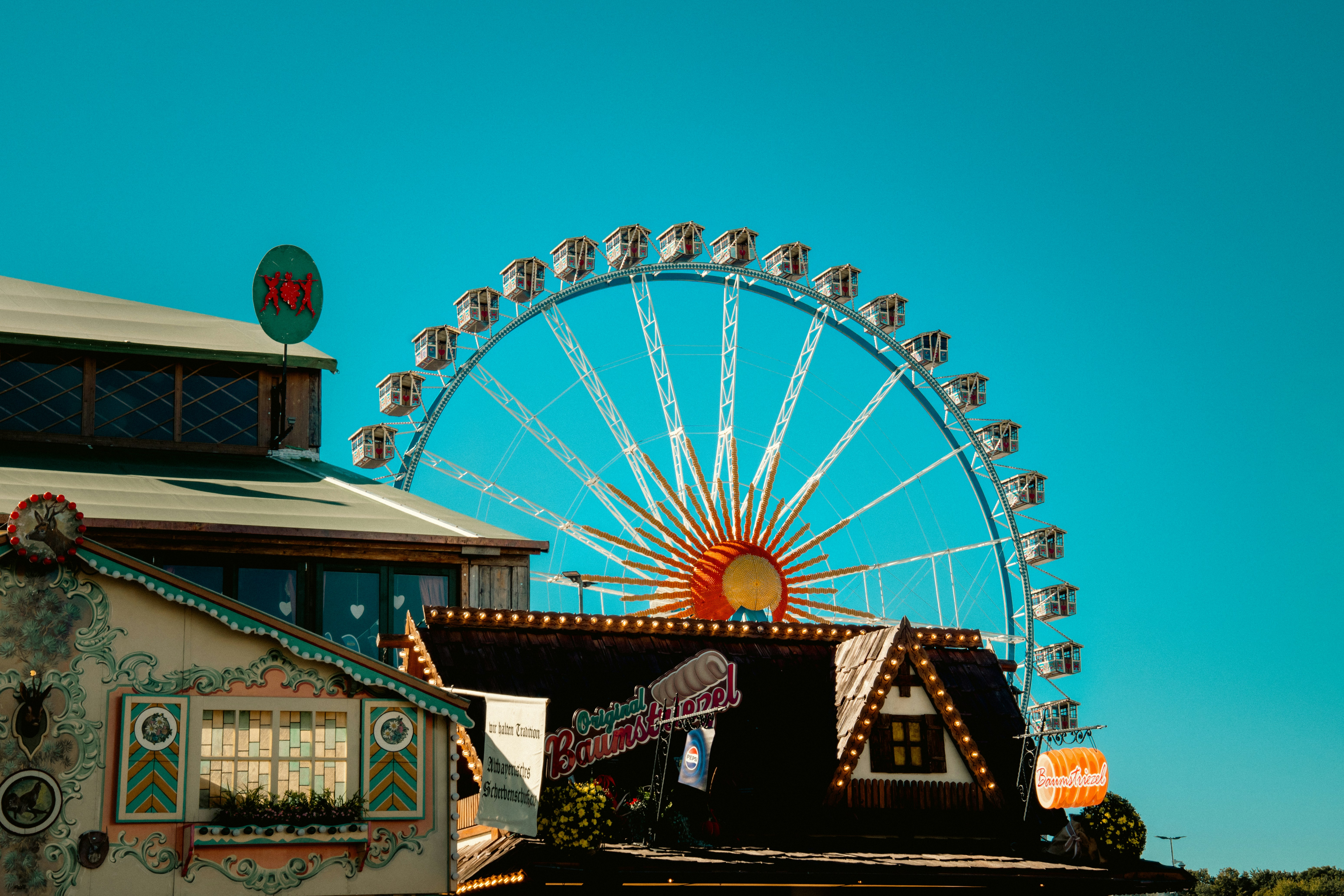 A large ferris wheel behind traditional wooden fairground buildings under a clear blue sky
