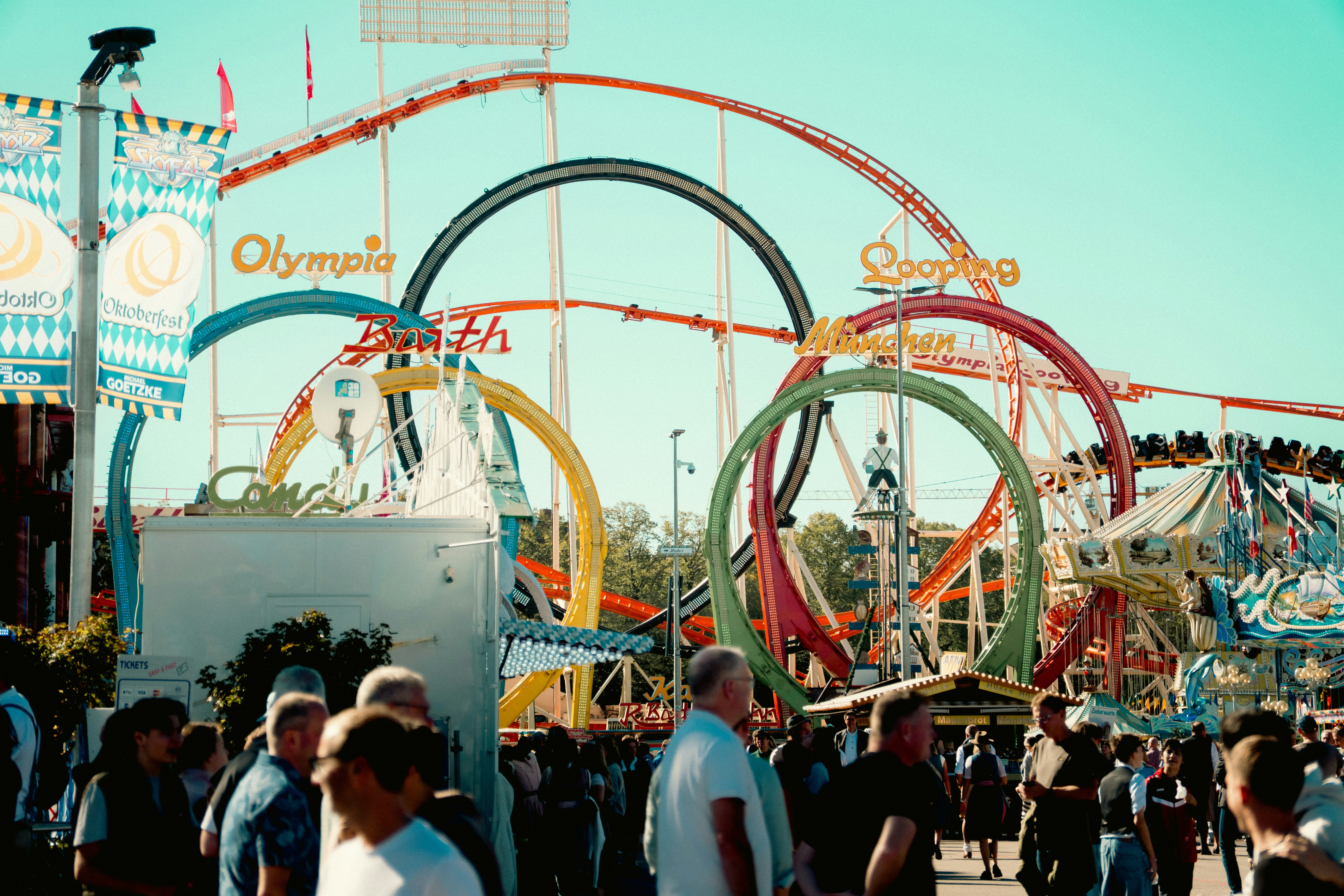 A crowd of people walking past the Olympia Looping roller coaster at Oktoberfest