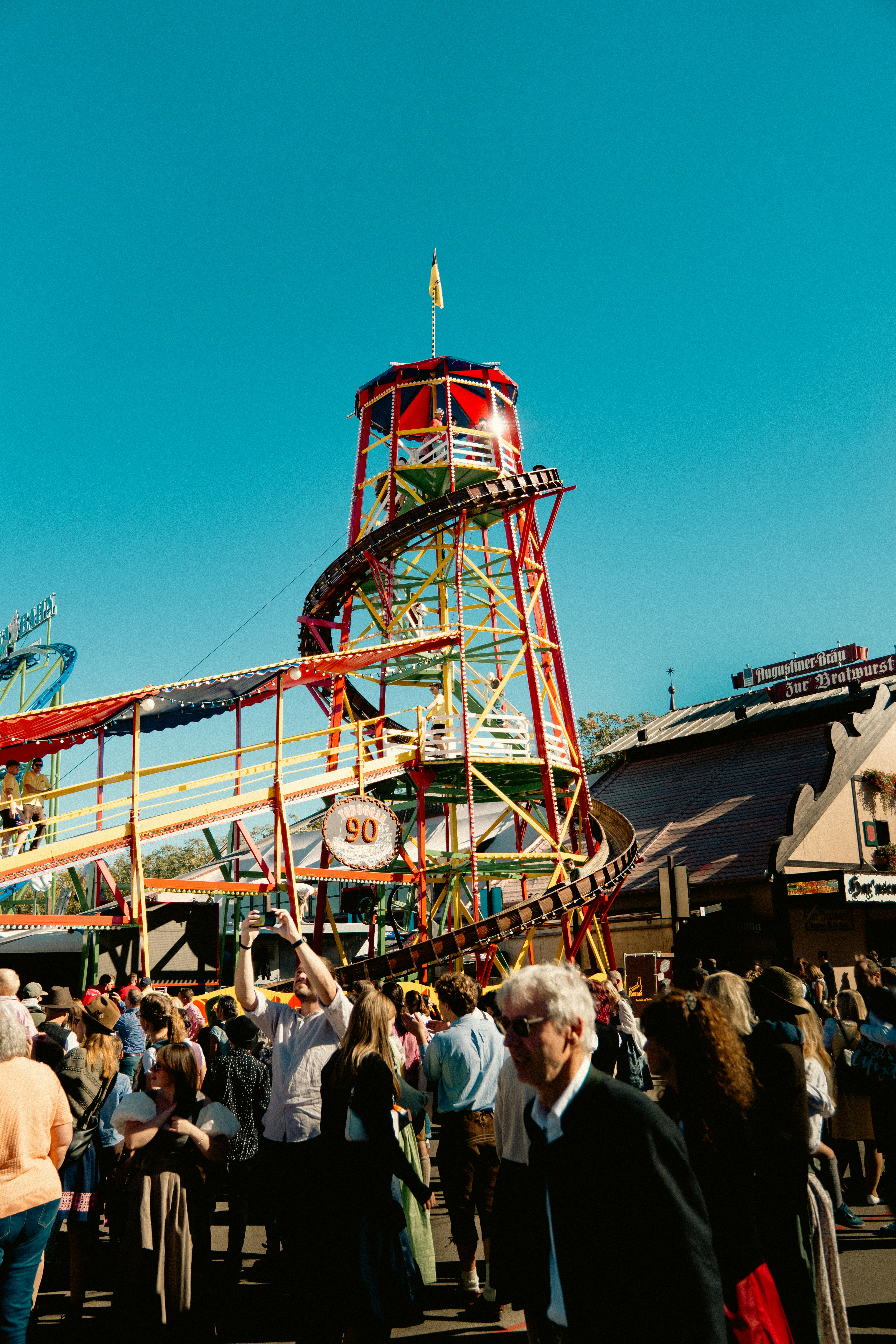 A crowd of people at a fairground with a tall spiral toboggan ride