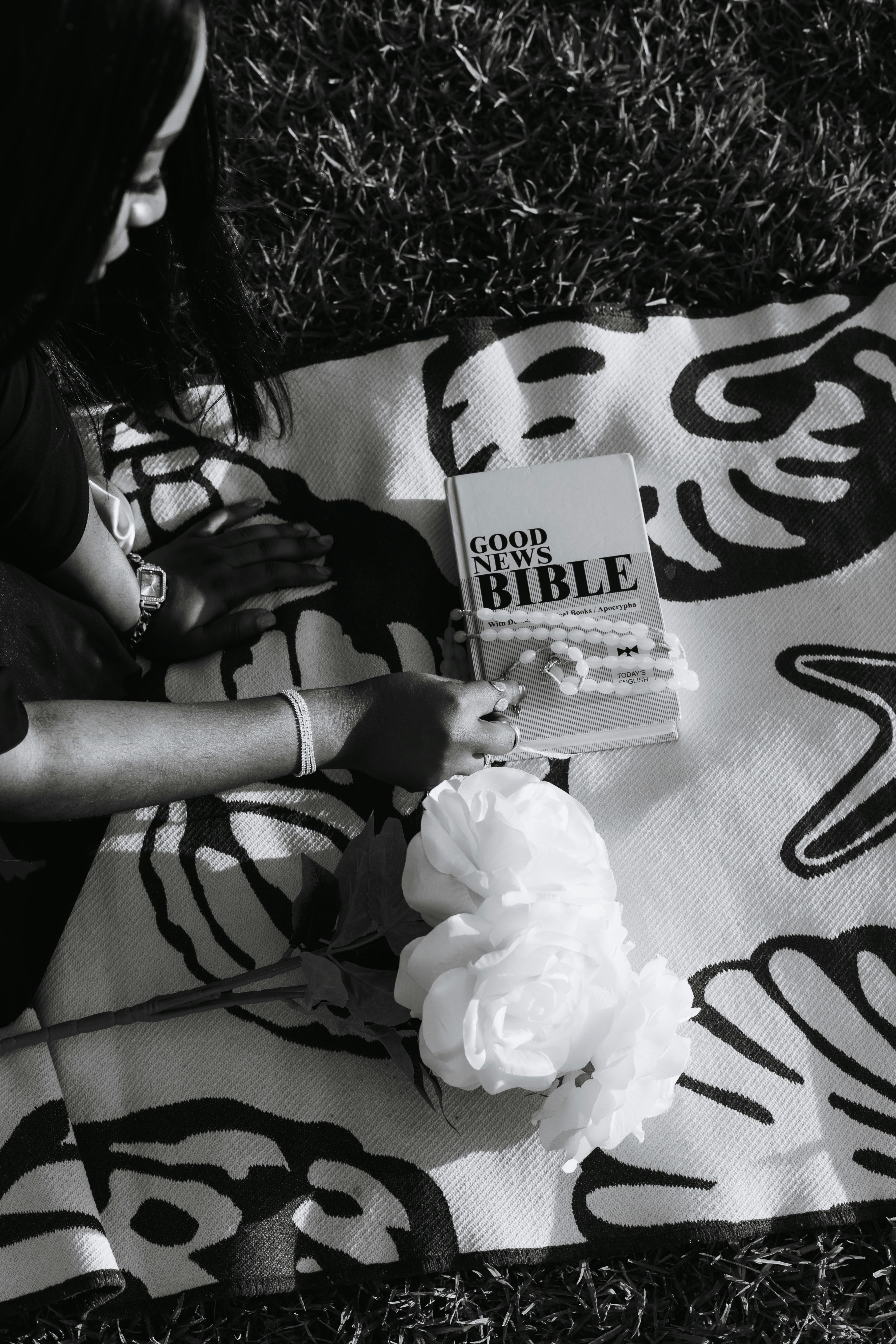 A person with a bible and white flowers on a patterned blanket outdoors