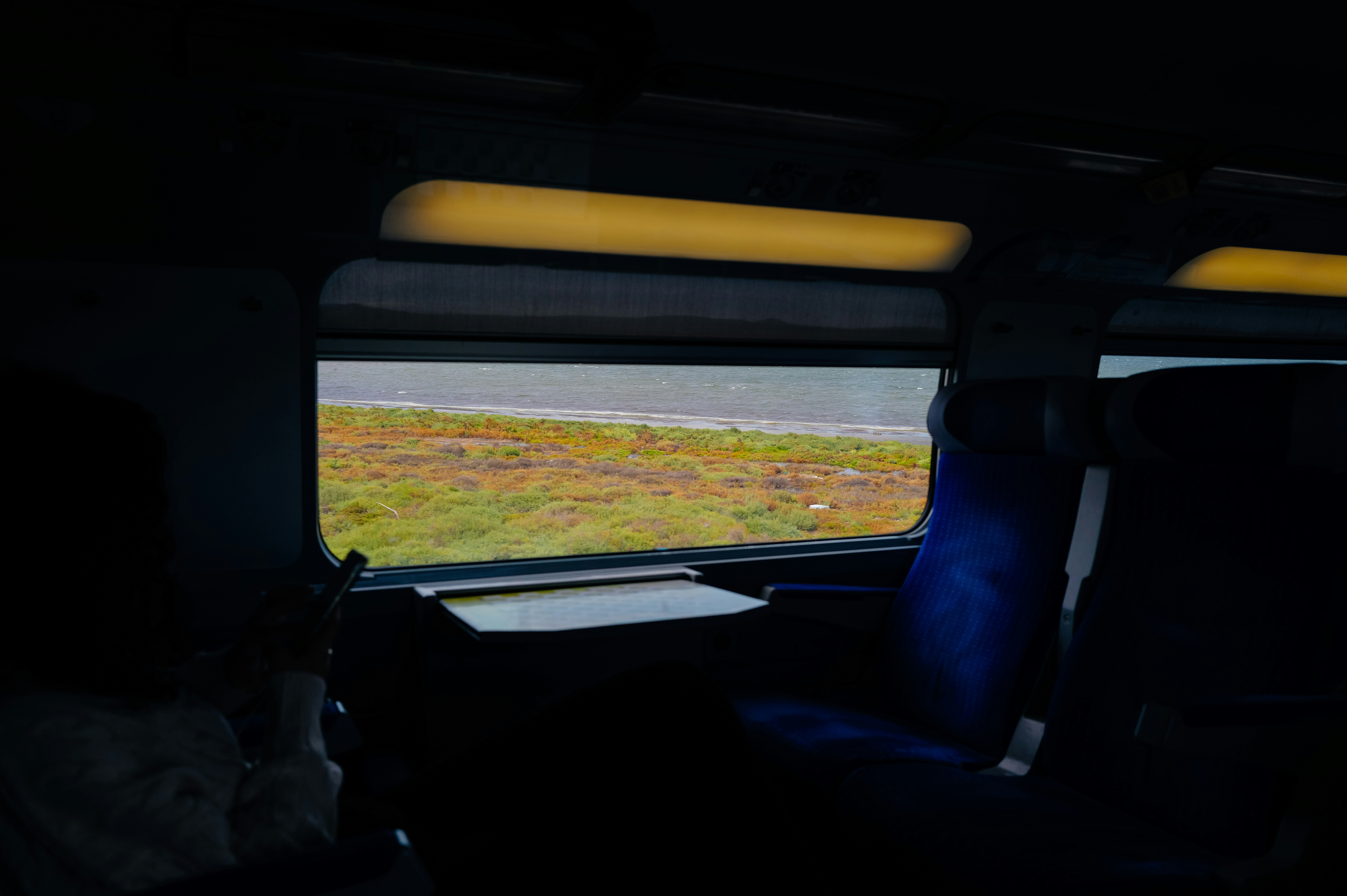 Uma vista de uma paisagem costeira de dentro de um vagão de trem pouco iluminado