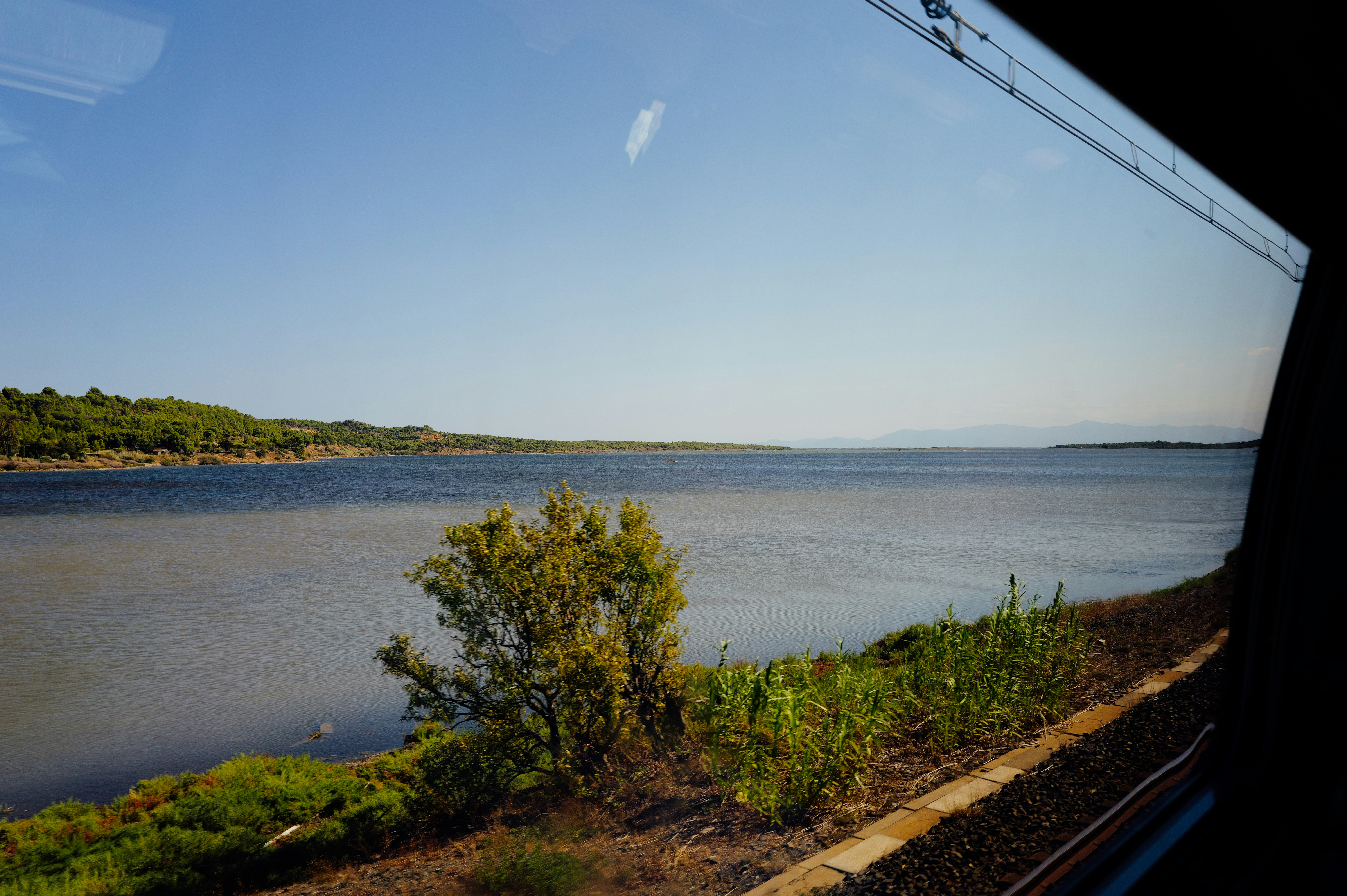 Uma vista de um lago calmo a partir da janela de um trem com vegetação verde à beira da costa