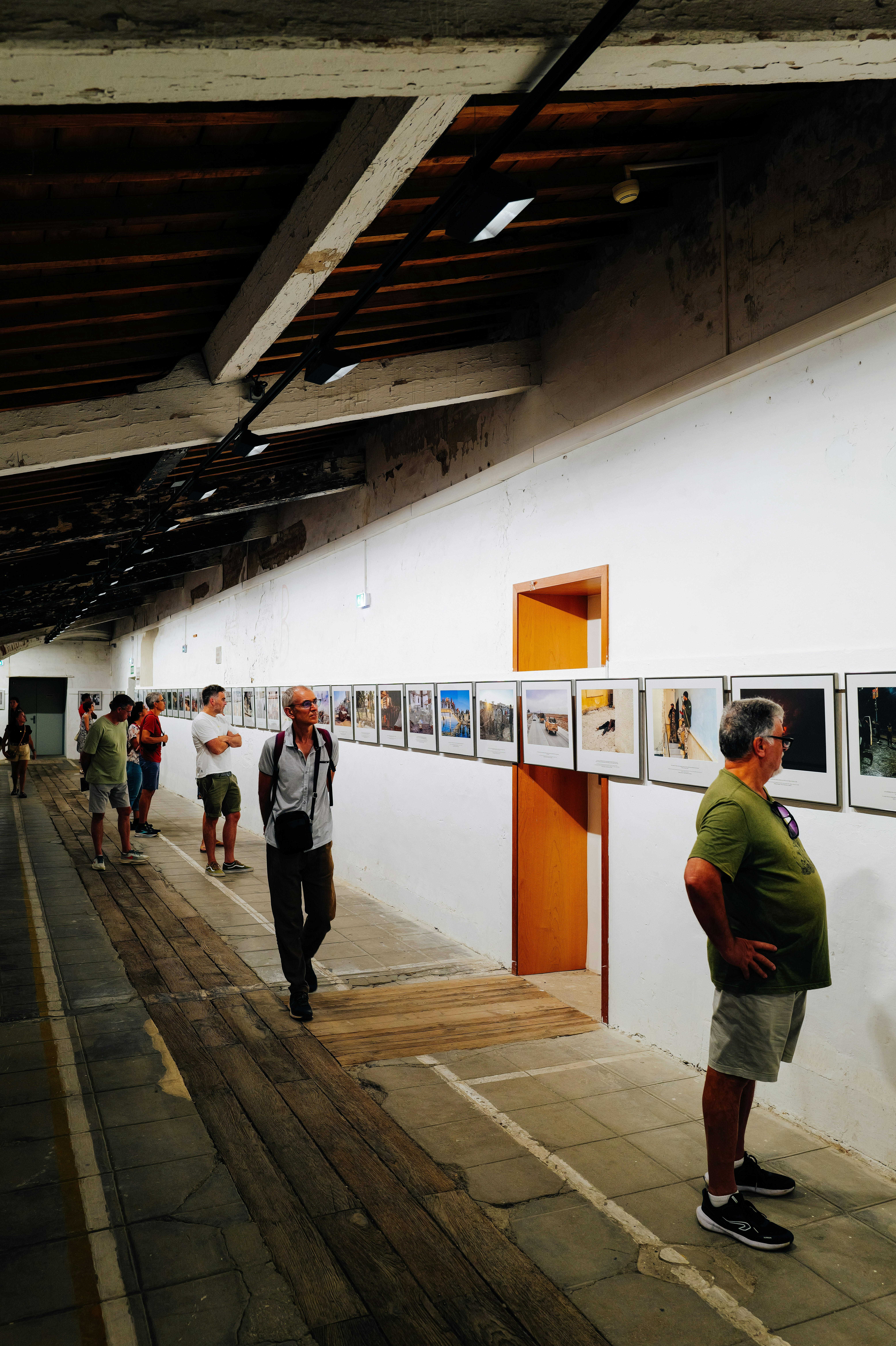 Pessoas caminhando por uma longa parede branca exibindo fotografias emolduradas em uma galeria