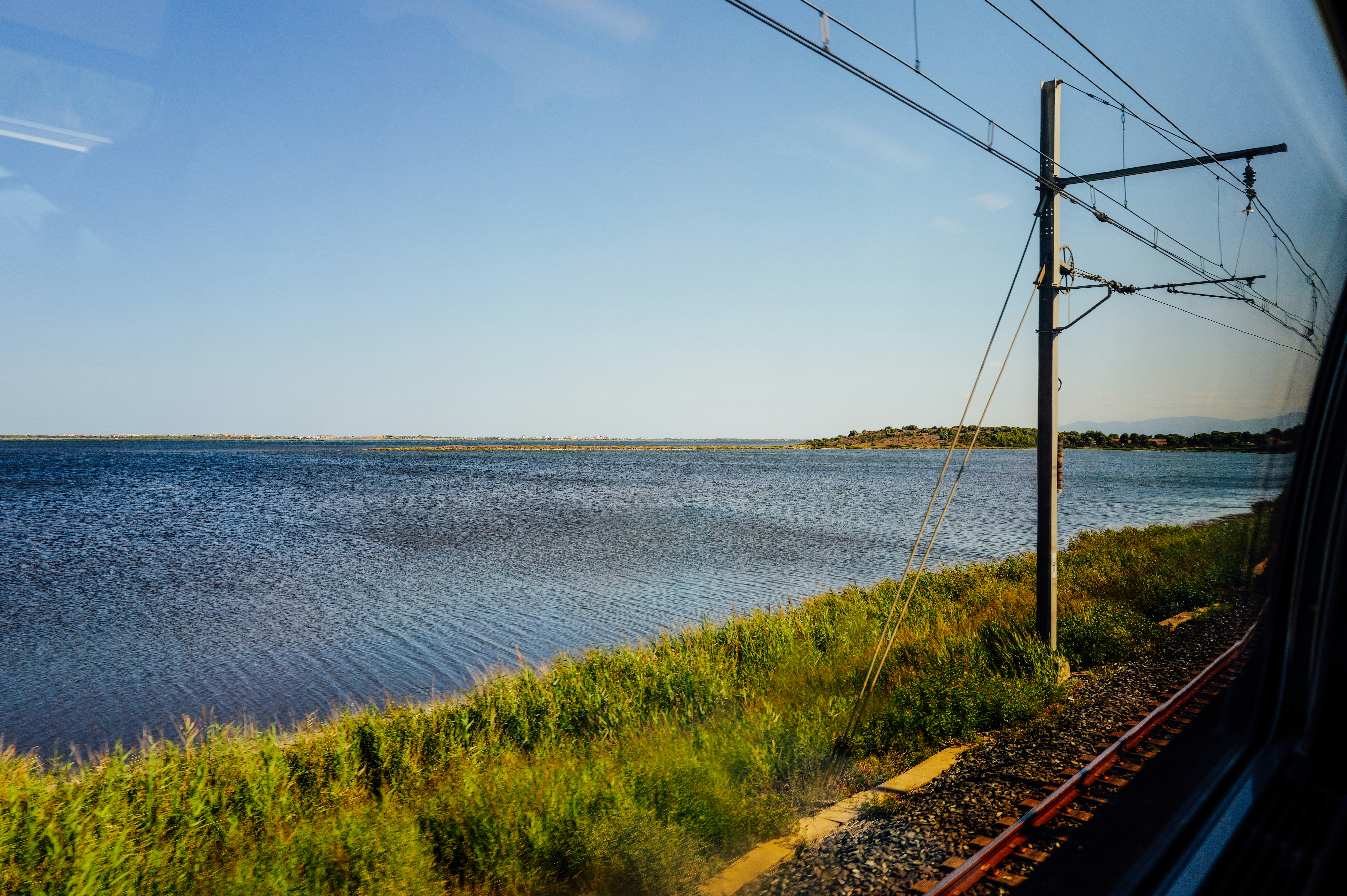 Vista da janela do trem de um lago calmo ao lado dos trilhos gramados