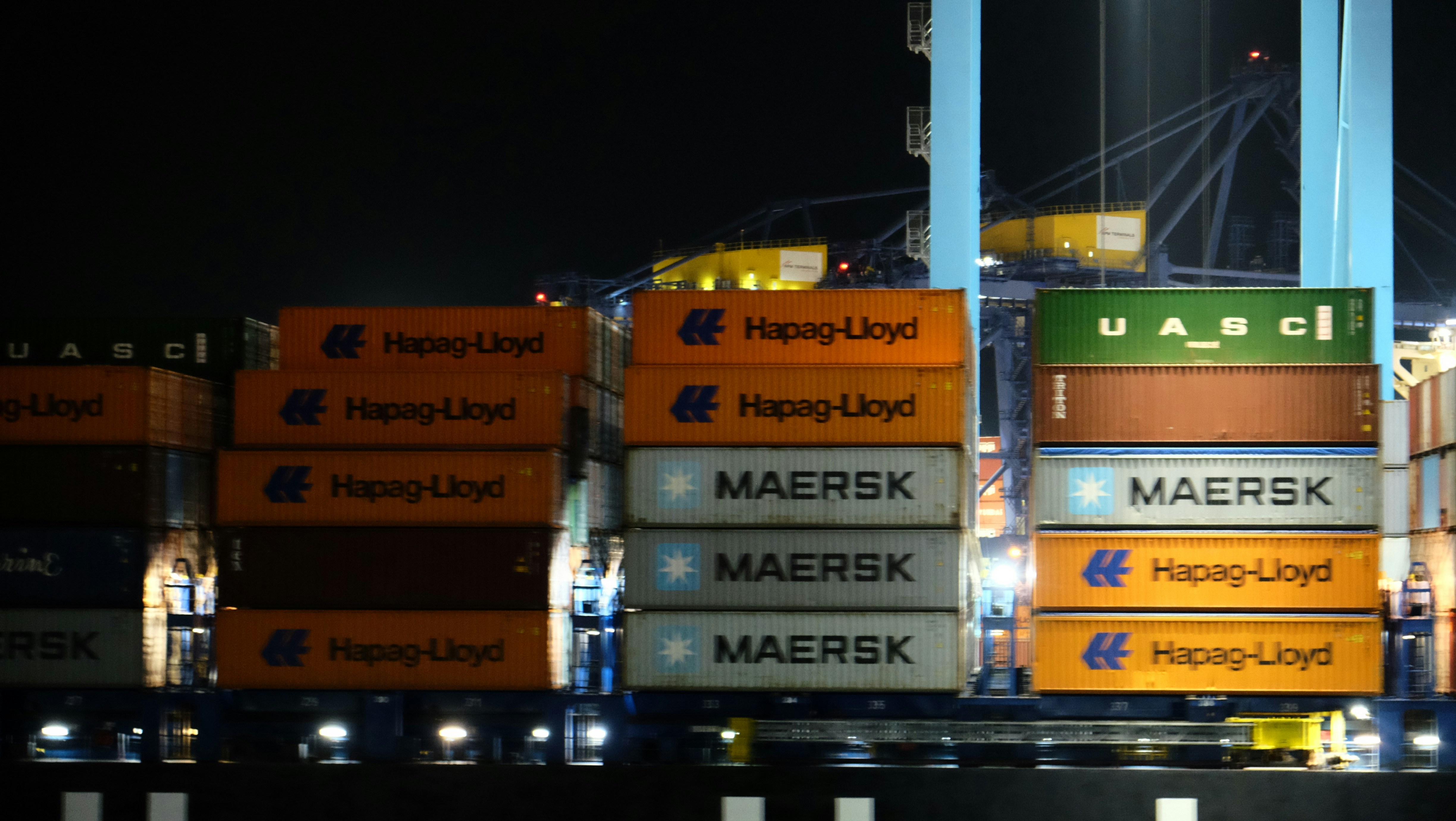 Conteneurs maritimes empilés avec les marques Hapag-Lloyd et Maersk dans un port la nuit