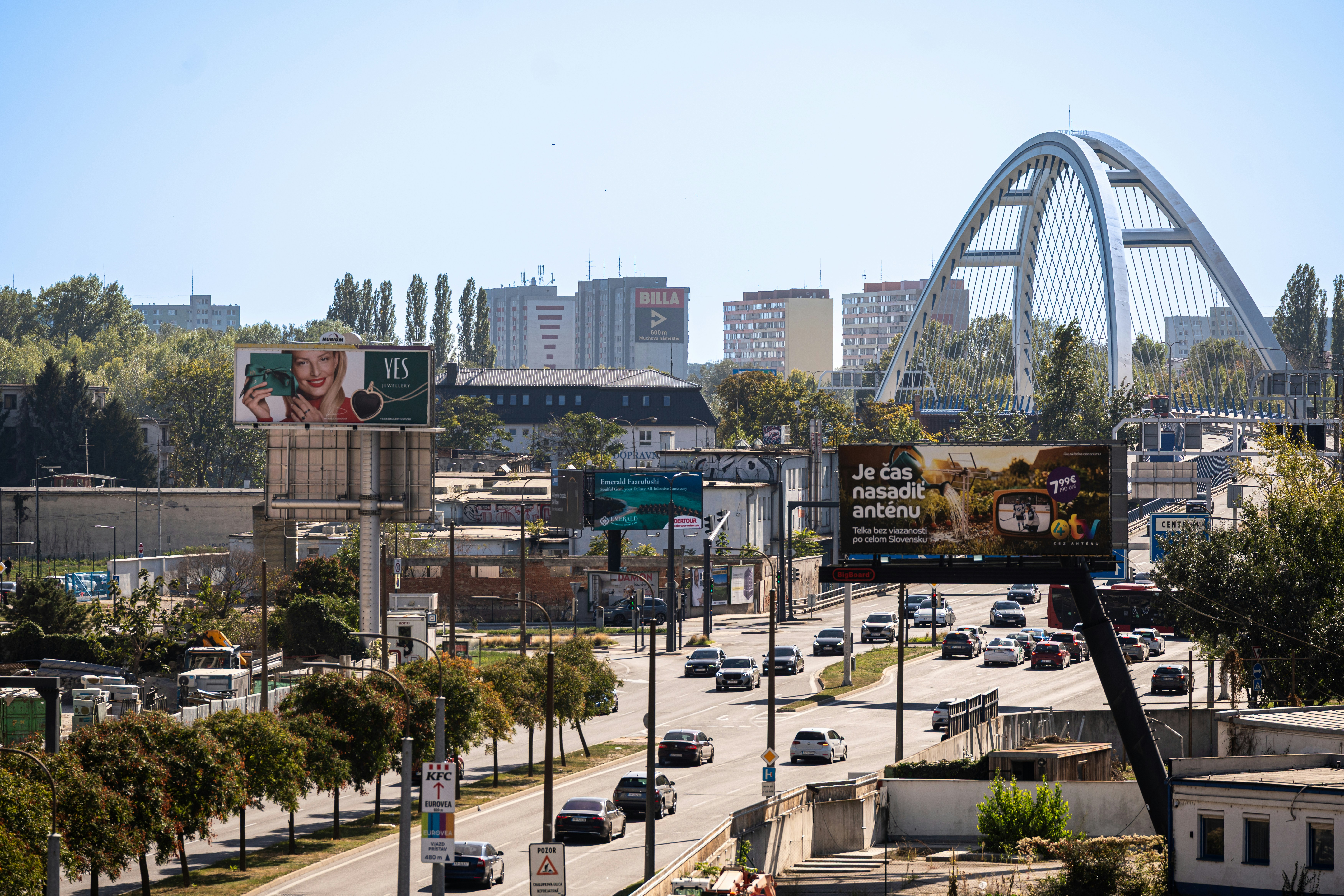 Cars driving on a multi-lane road near a large arched bridge in Bratislava
