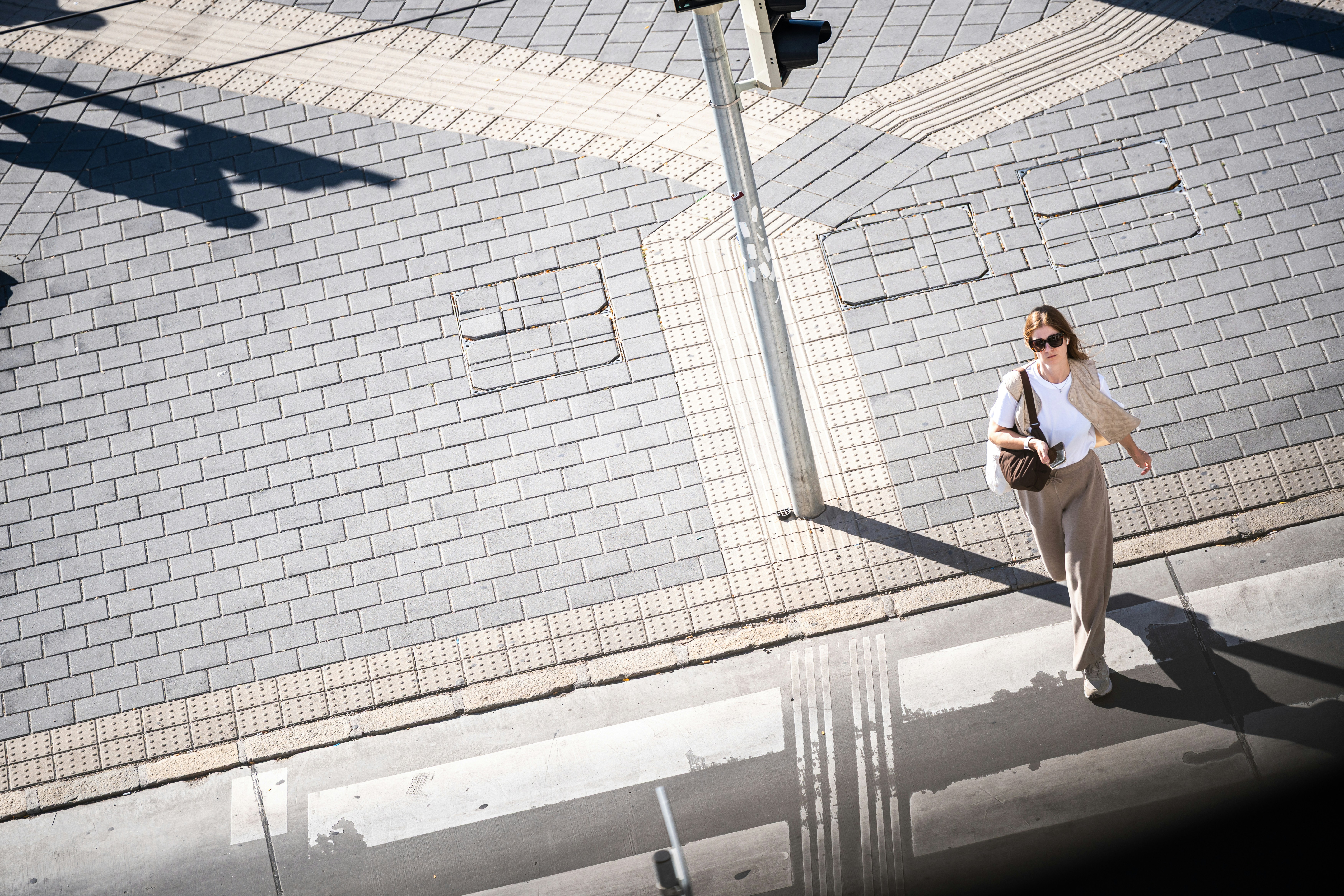A woman in sunglasses walking across a paved city intersection in bright sunlight