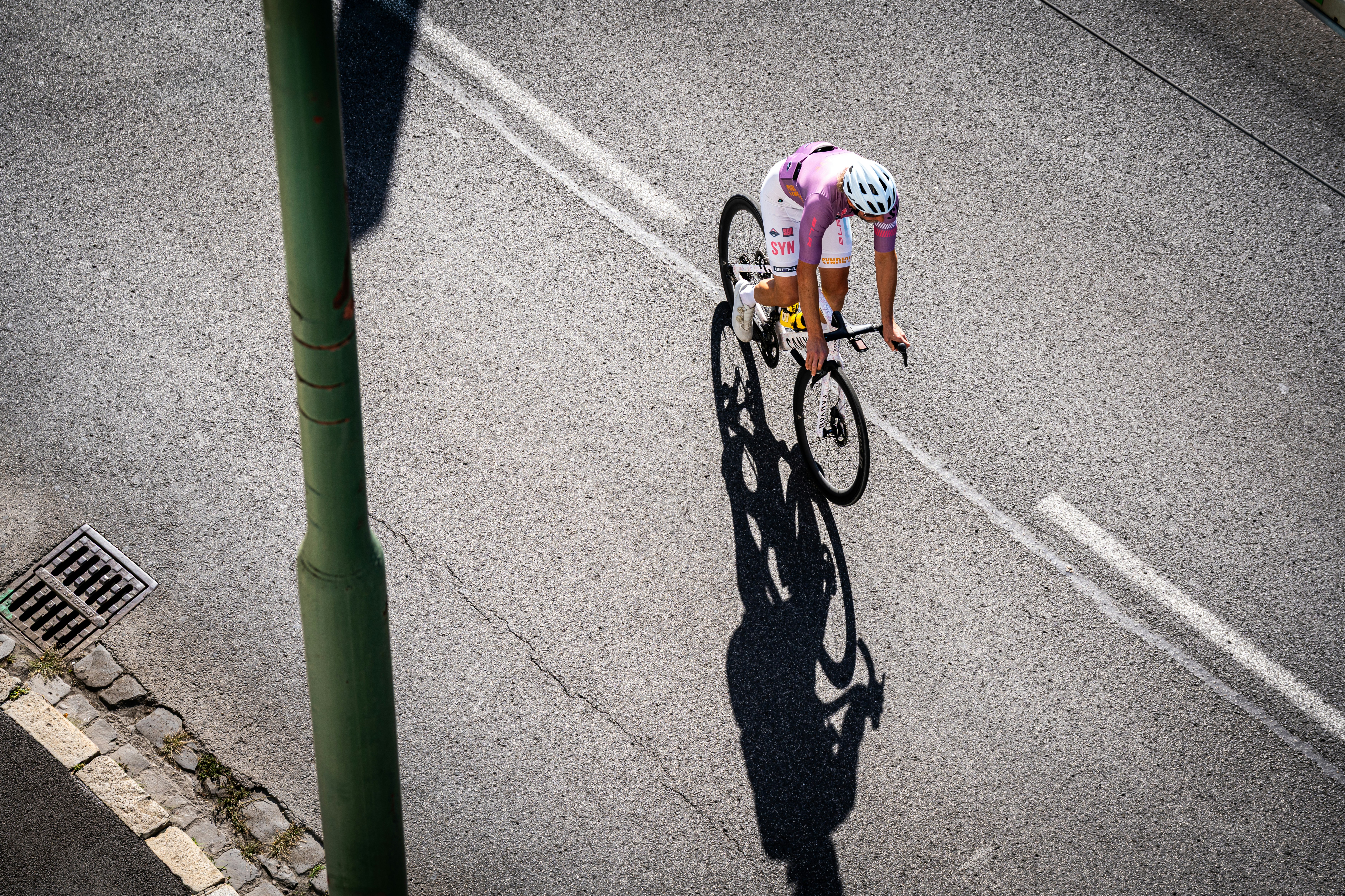 A cyclist in a white and purple jersey riding on an asphalt road
