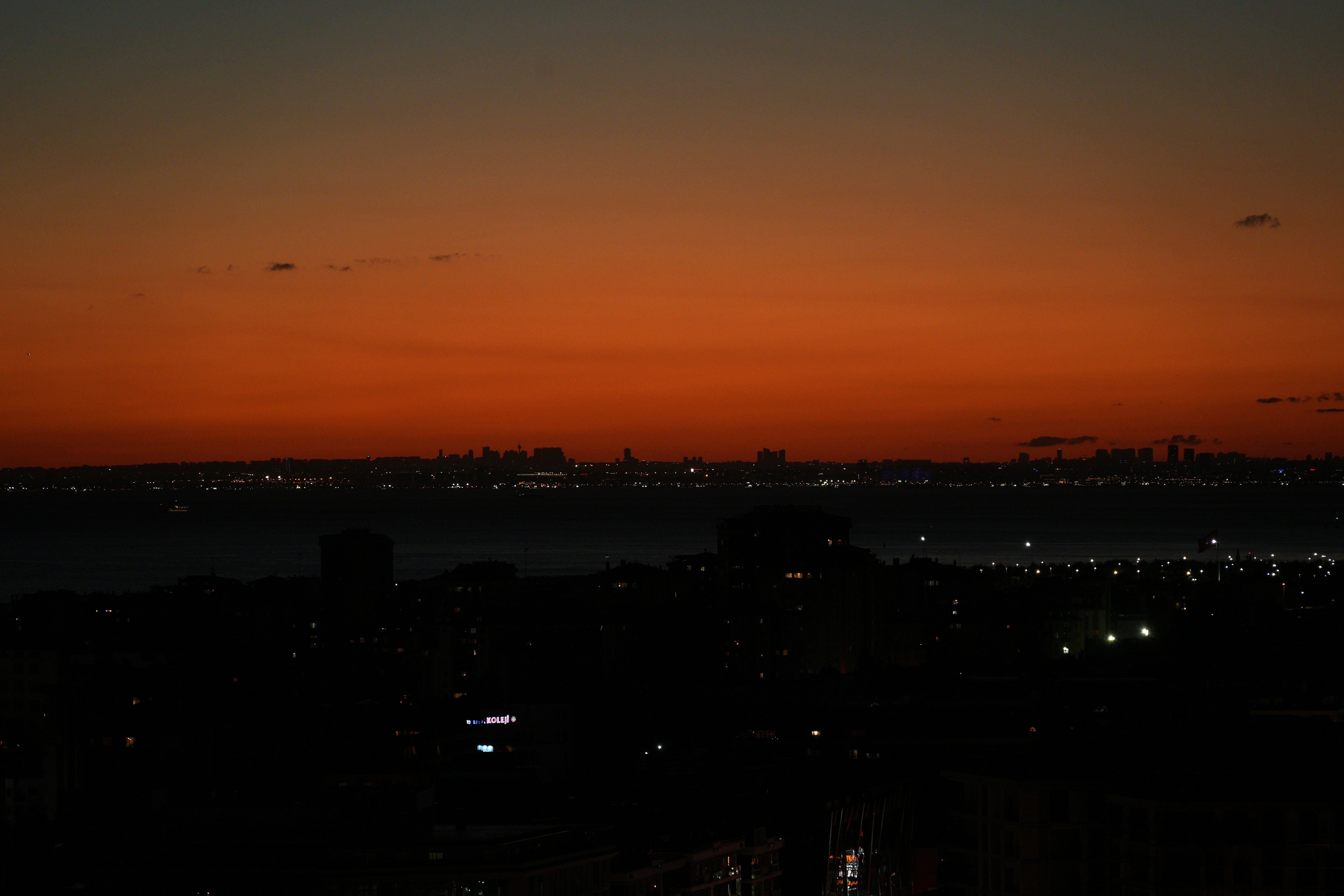 A dark city skyline across a body of water under a warm orange sky