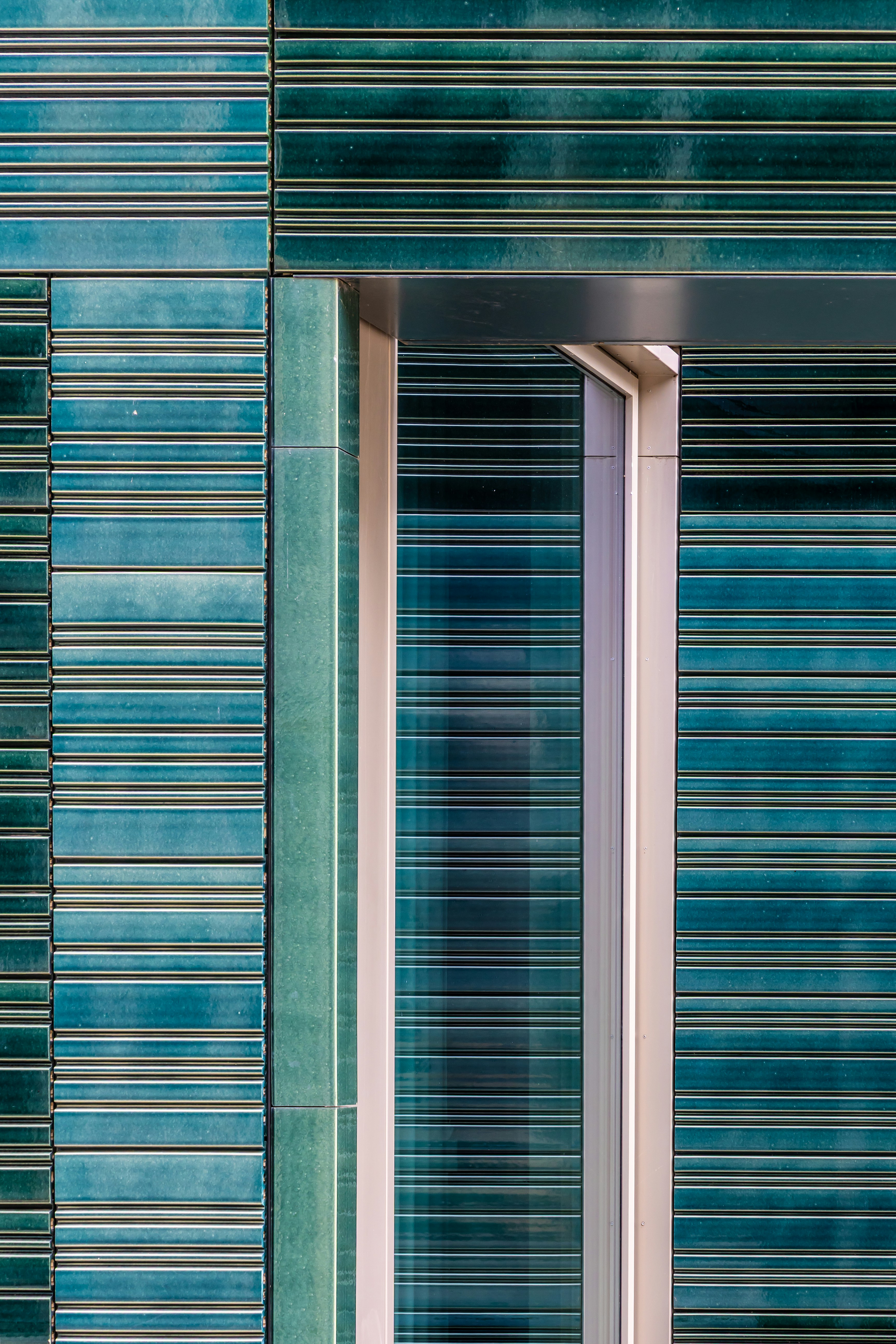 Fasad bangunan modern dengan ubin keramik horizontal teal dan jendela cekung