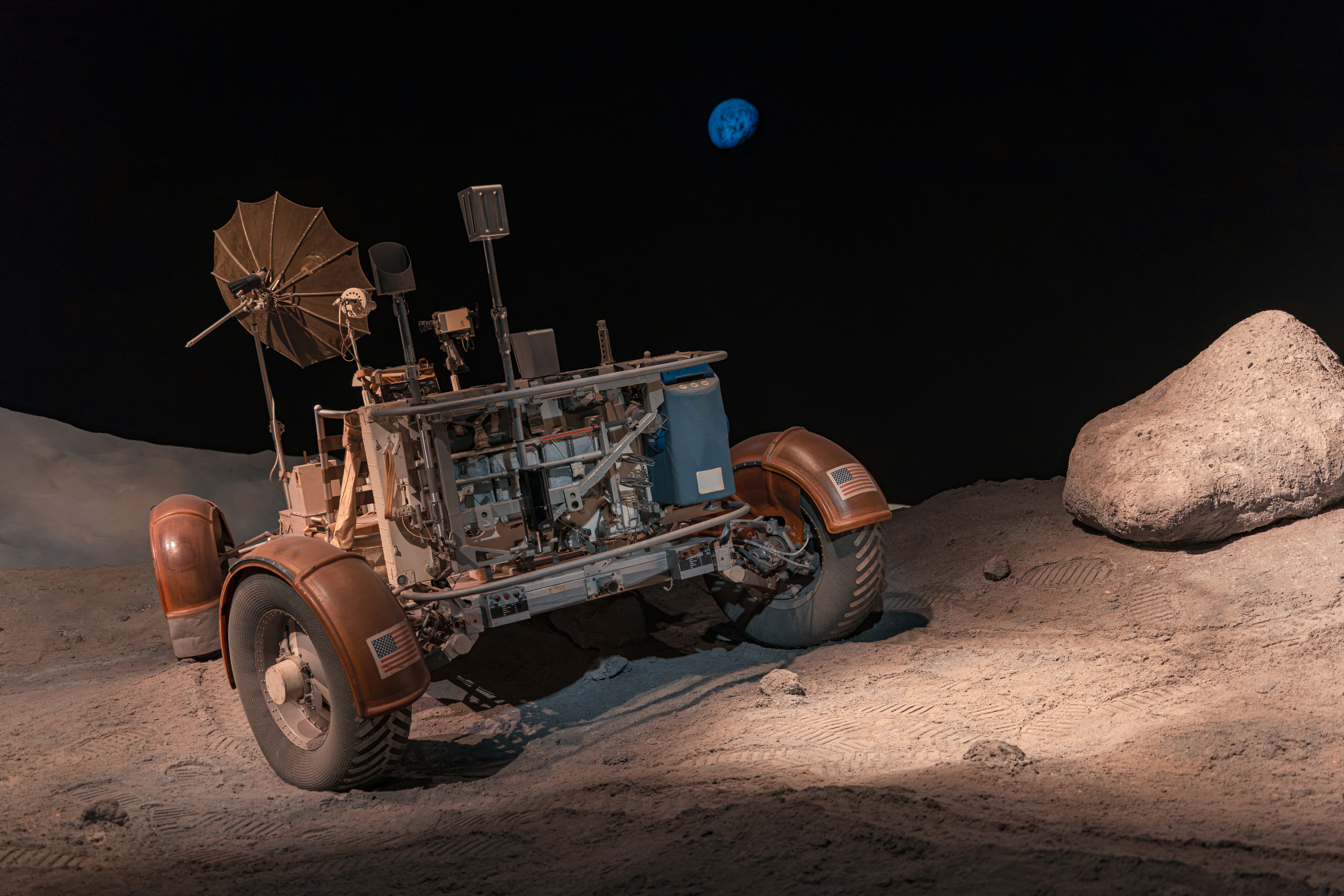Un rover lunar sobre una superficie gris polvorienta con un planeta azul distante