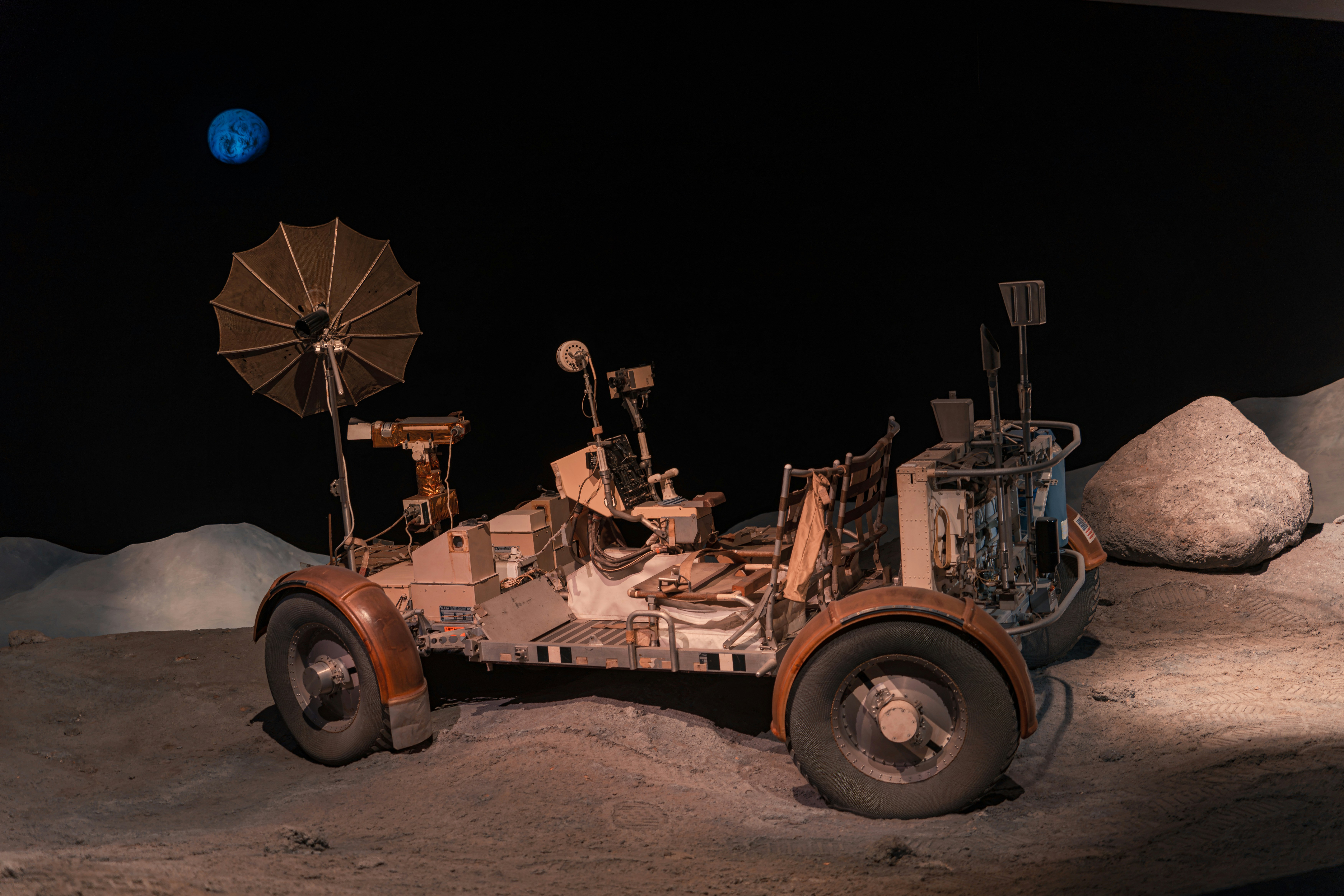 Un rover lunar sobre una superficie gris con cráteres y una tierra azul en el cielo