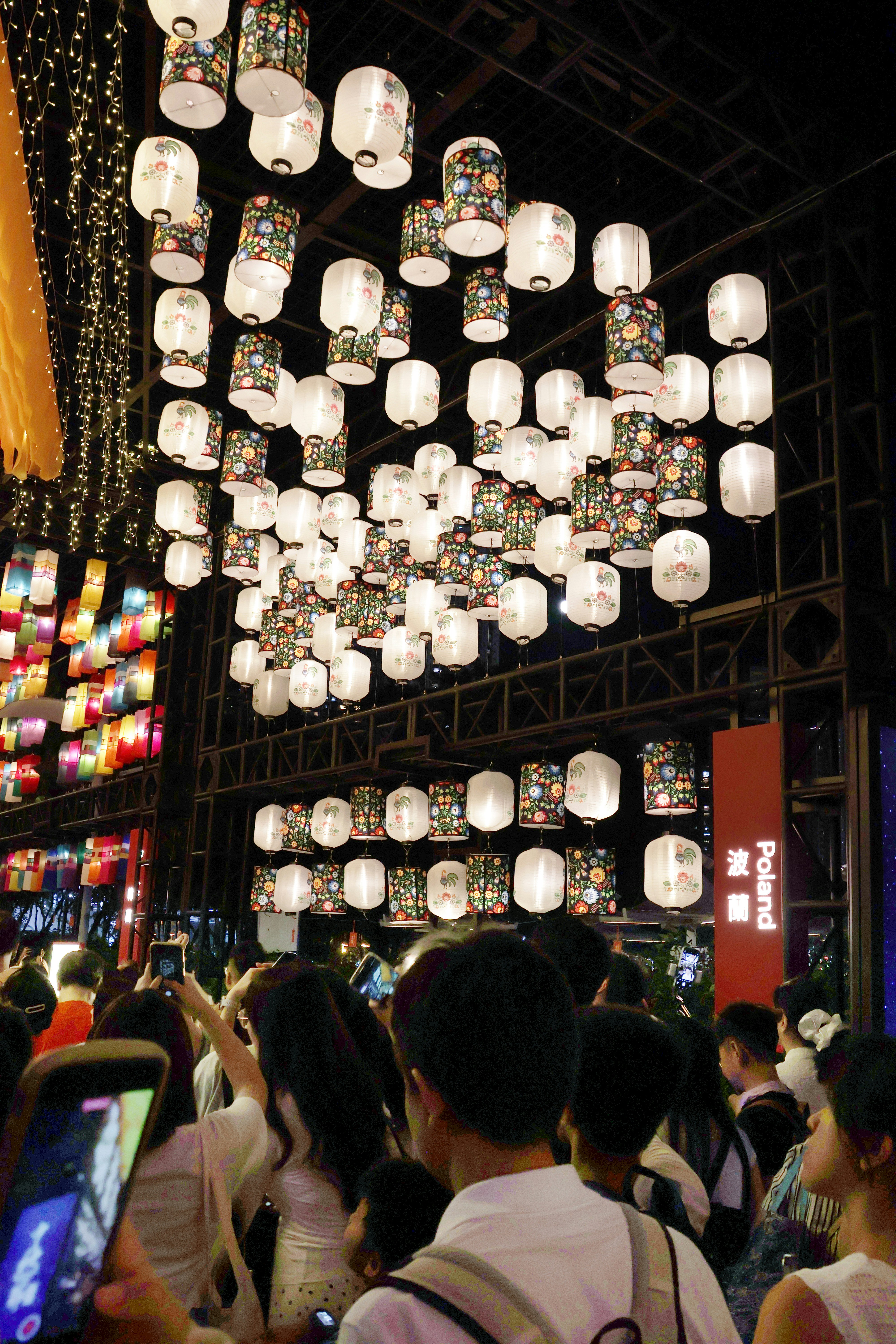 A crowd of people photographing hanging floral lanterns at a night festival