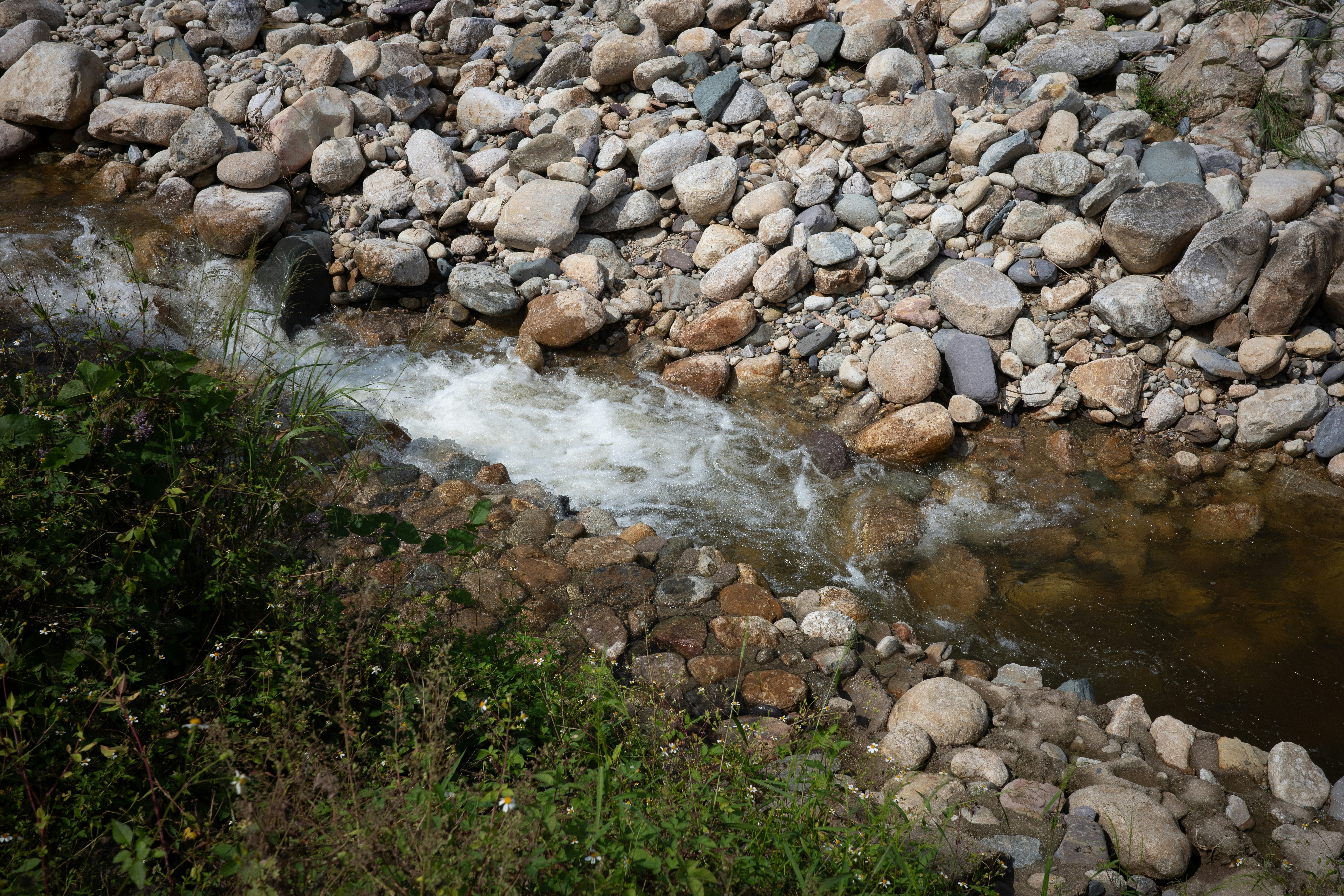 A small stream flowing over smooth river stones beside a grassy bank