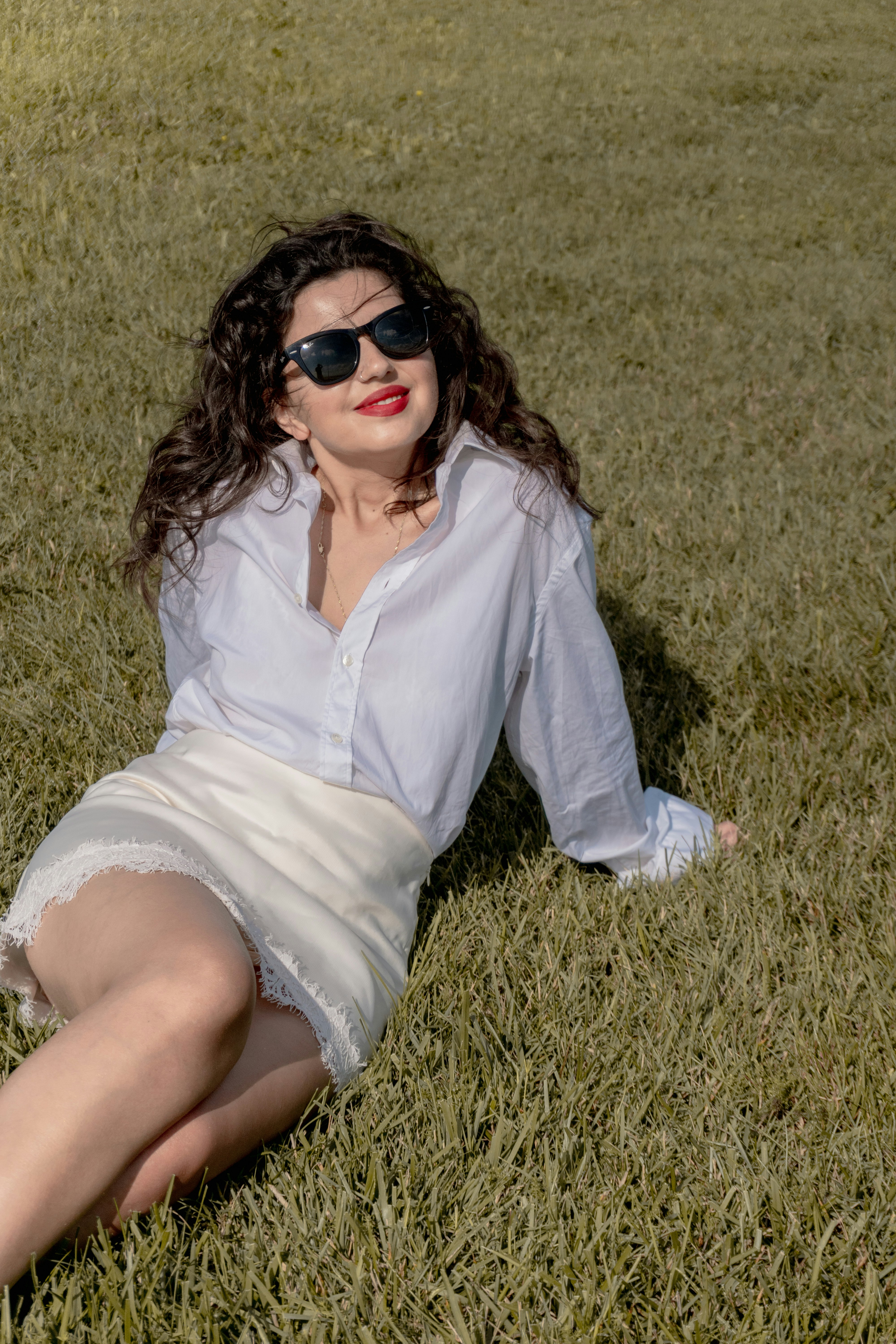 Seated in a white shirt dress, looking past the camera