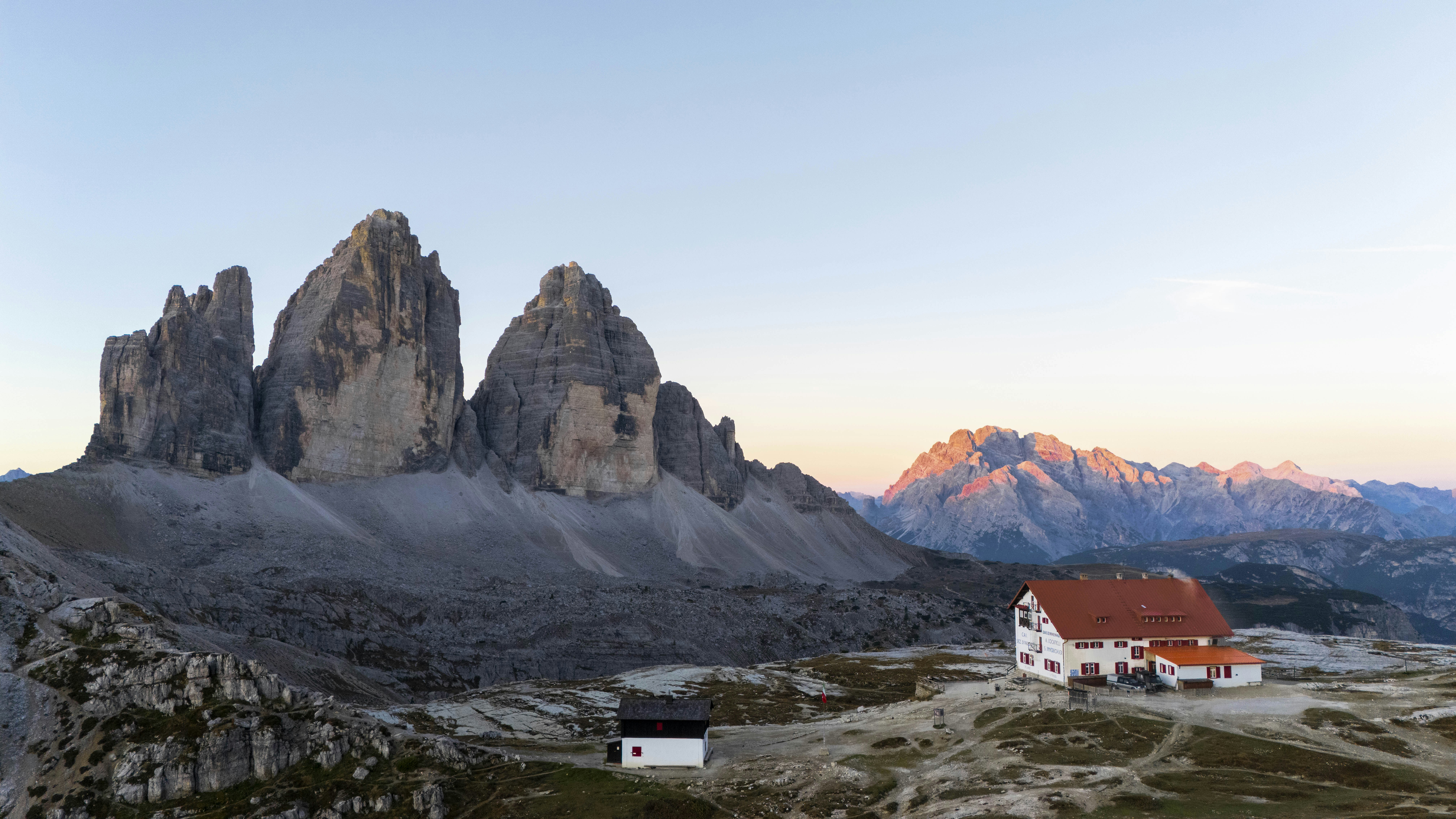 A mountain hut with a red roof below the Tre Cime di Lavaredo peaks