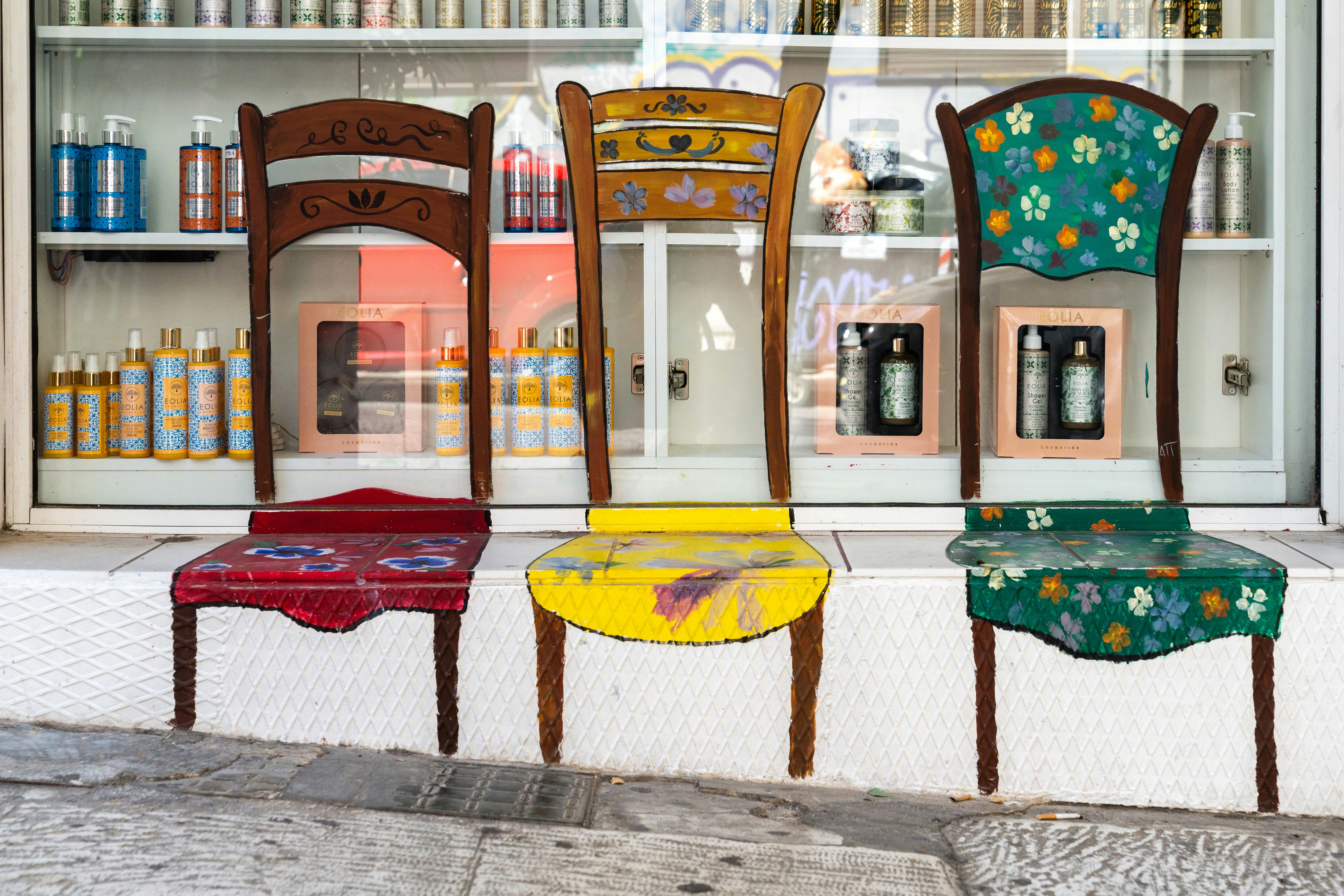 Three painted chairs on a storefront ledge in front of cosmetic products