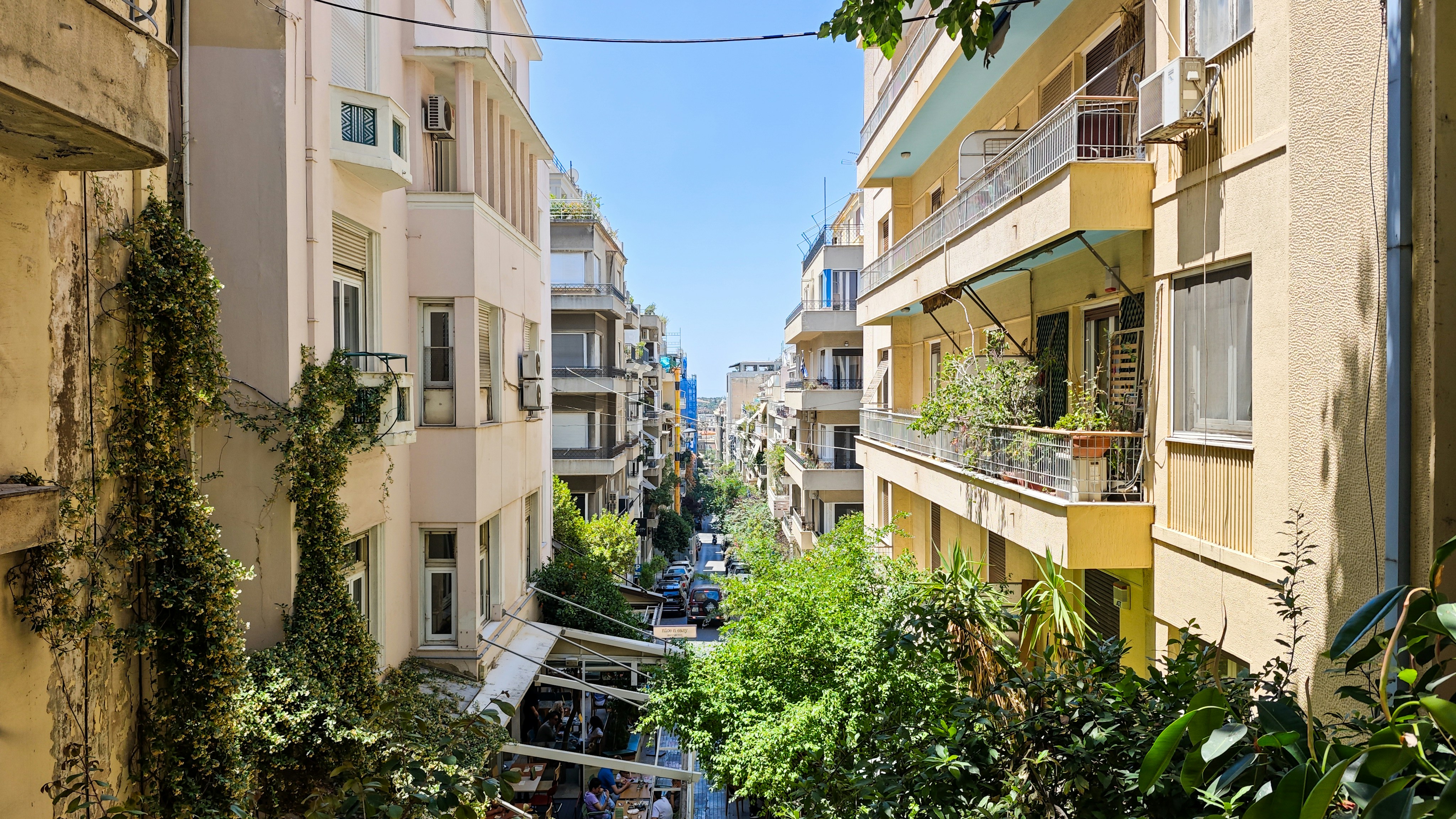 A narrow street between tall apartment buildings with balconies and climbing vines
