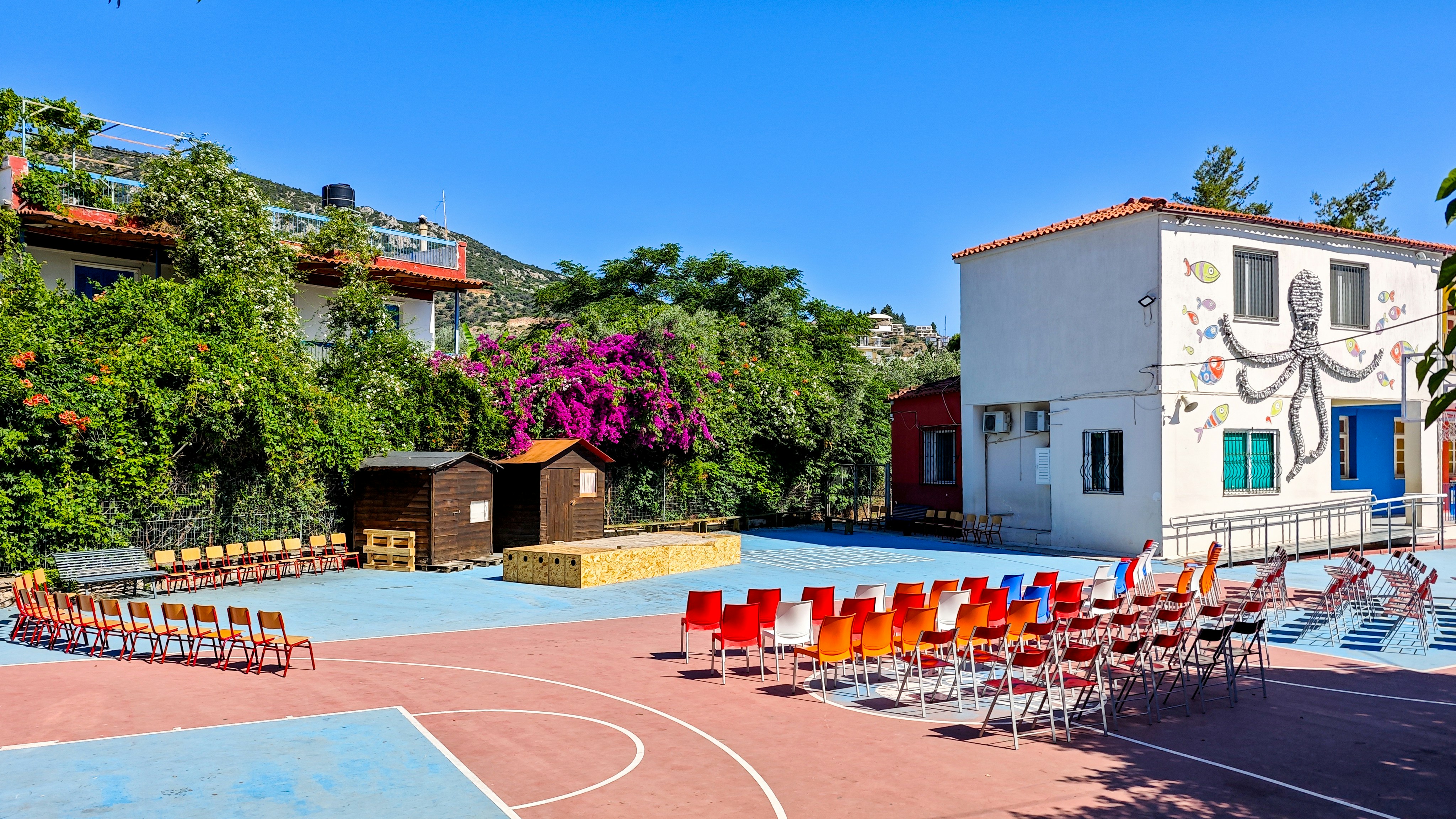 Rows of colorful chairs arranged on a paved outdoor court with a building mural