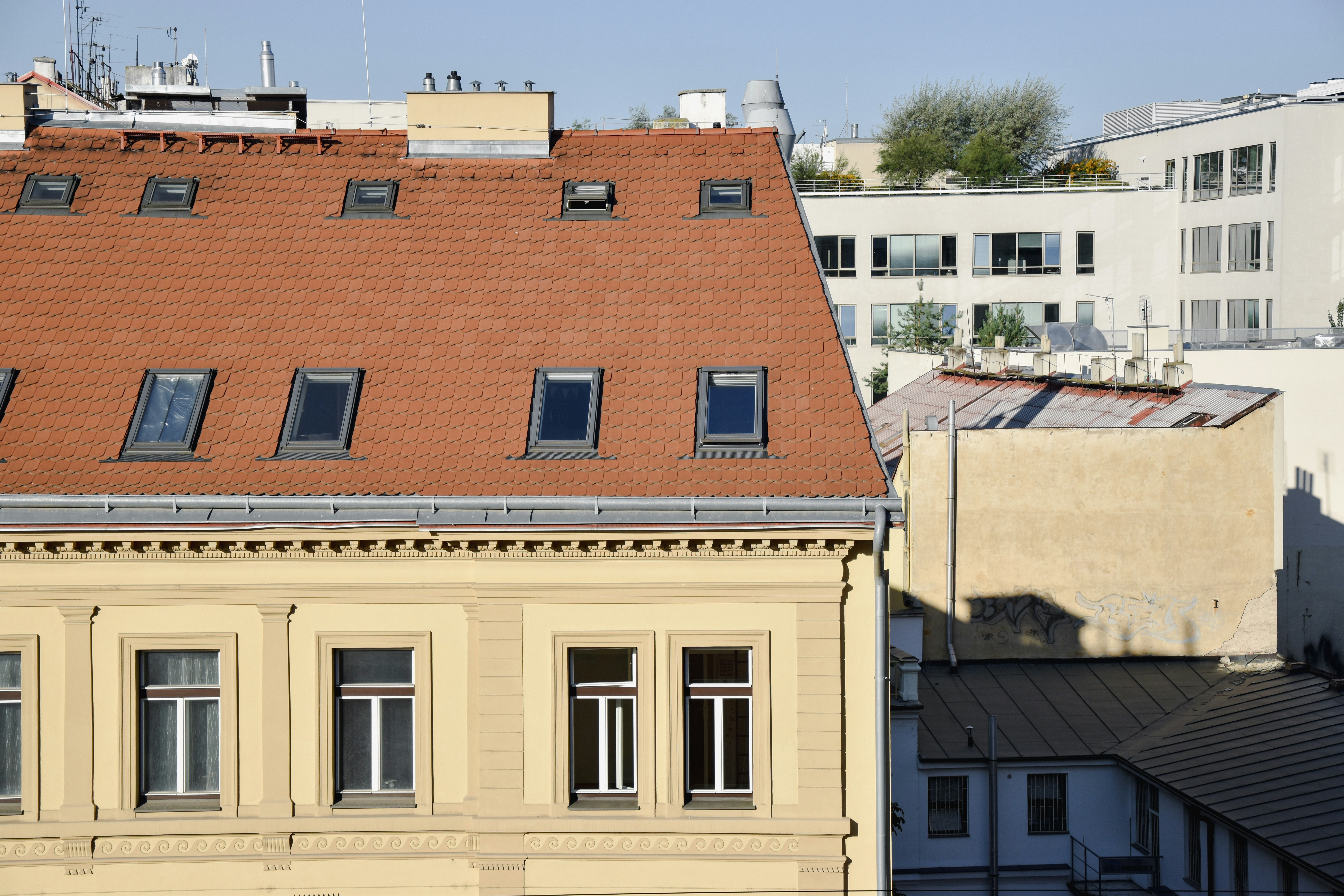 A yellow building with a red tiled roof and skylights in an urban setting