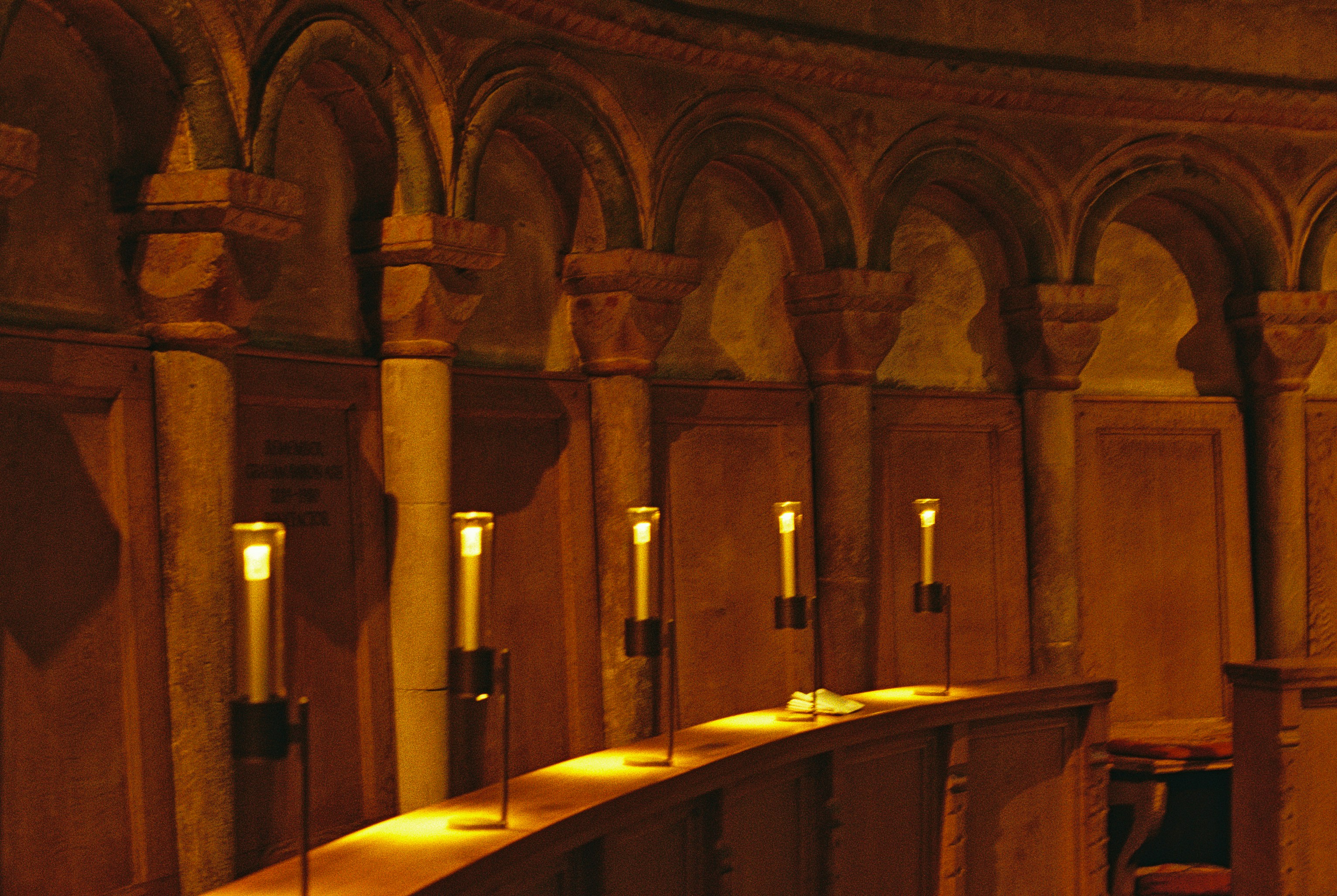 Five electric candles on a wooden ledge before stone arches in a dim room