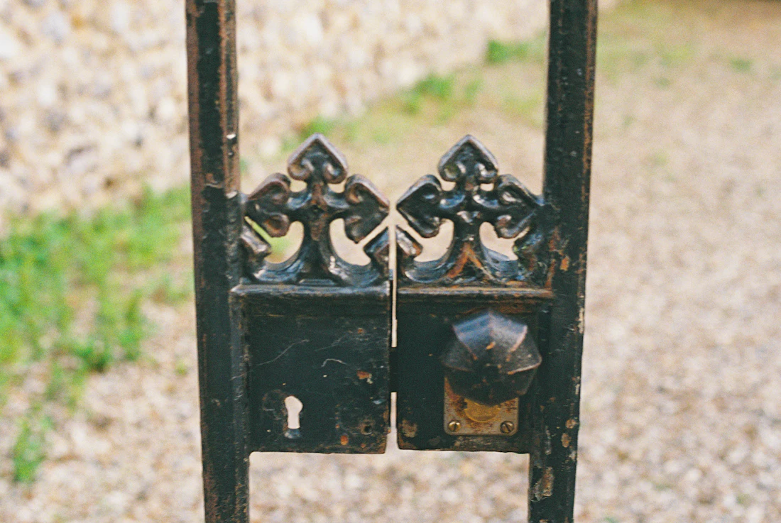 Black wrought iron gate with decorative top on a gravel drive