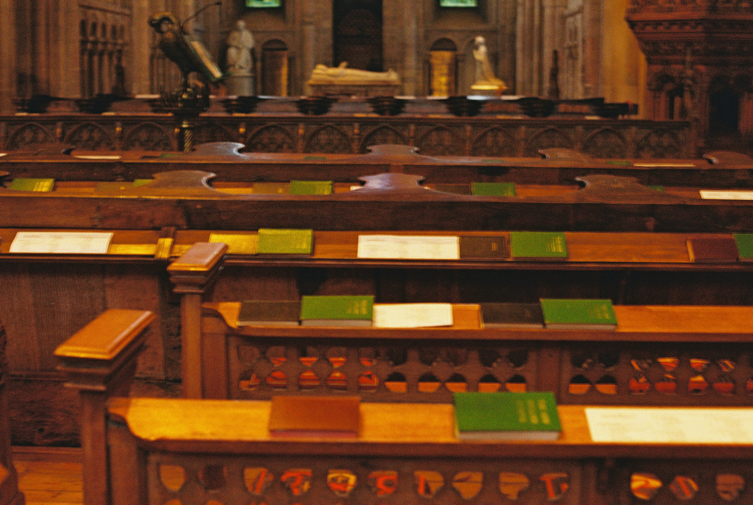 Rows of wooden church pews with green books and white papers in a cathedral