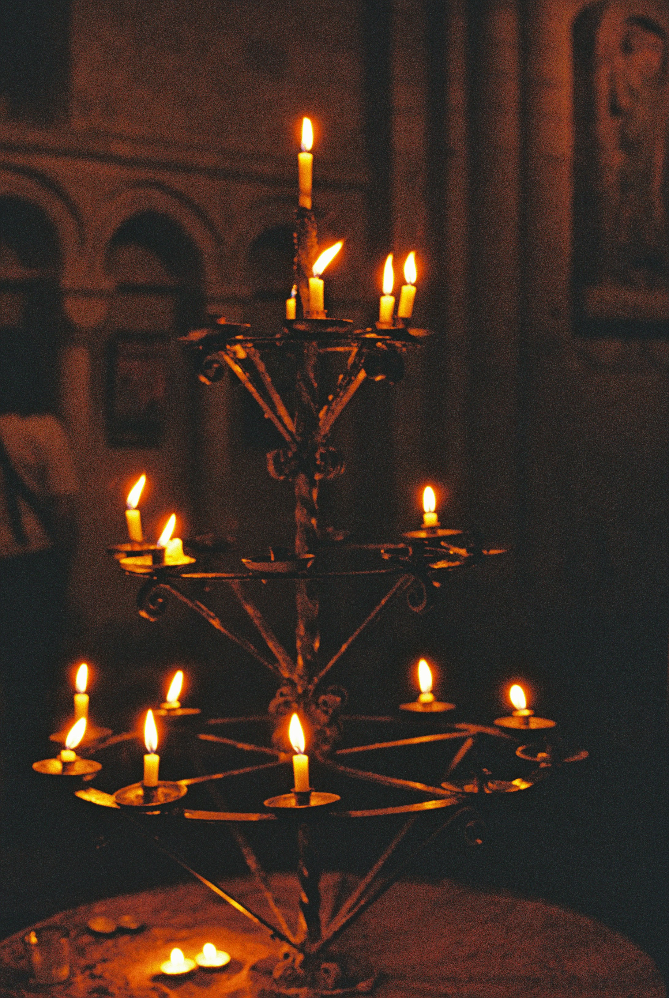 A tiered metal candle stand with many lit candles in a dark interior - 相关推荐