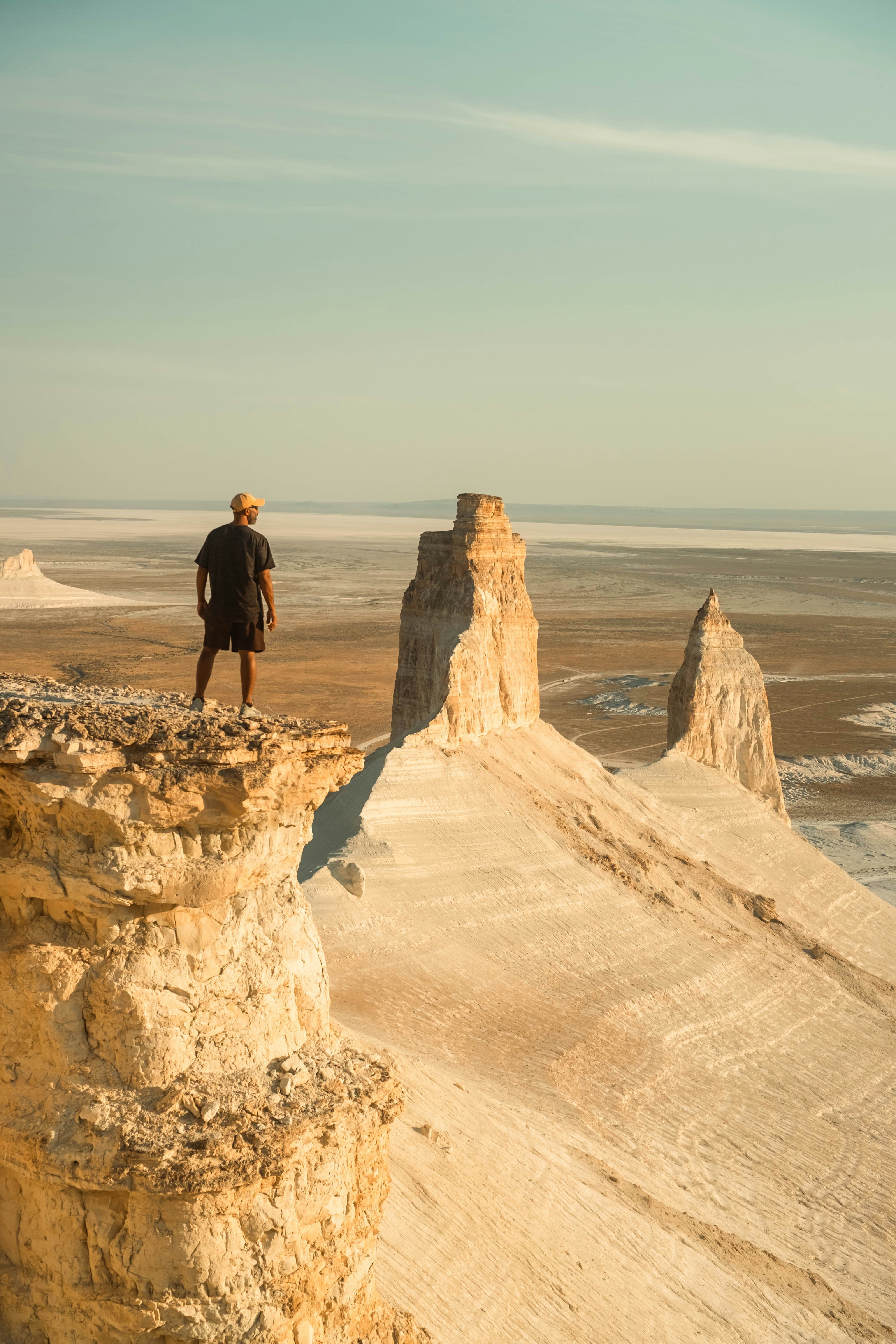 A person in a dark t-shirt and cap on a rocky cliff overlooking desert