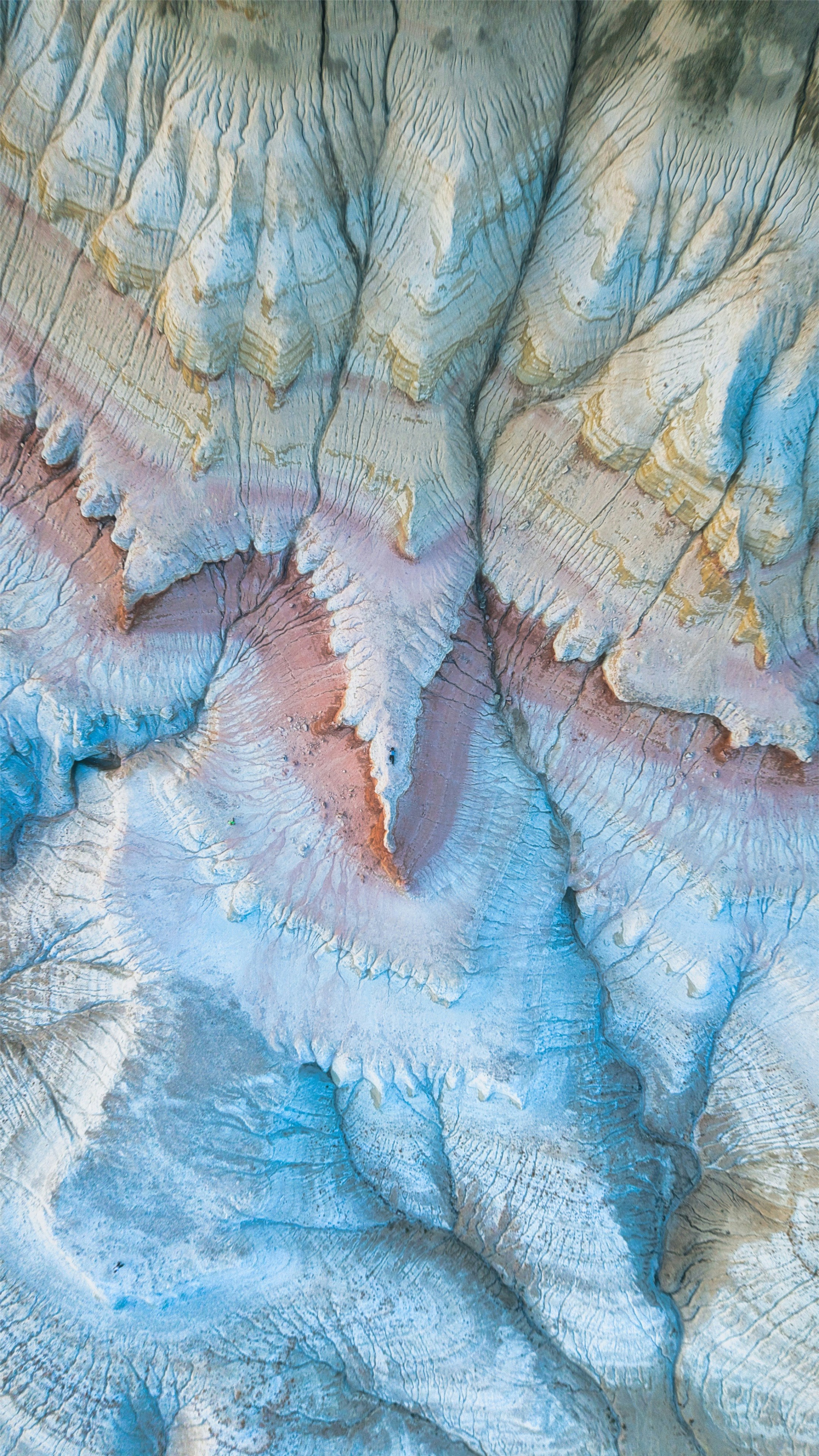 An aerial view of eroded blue and pink clay hills with deep ridges