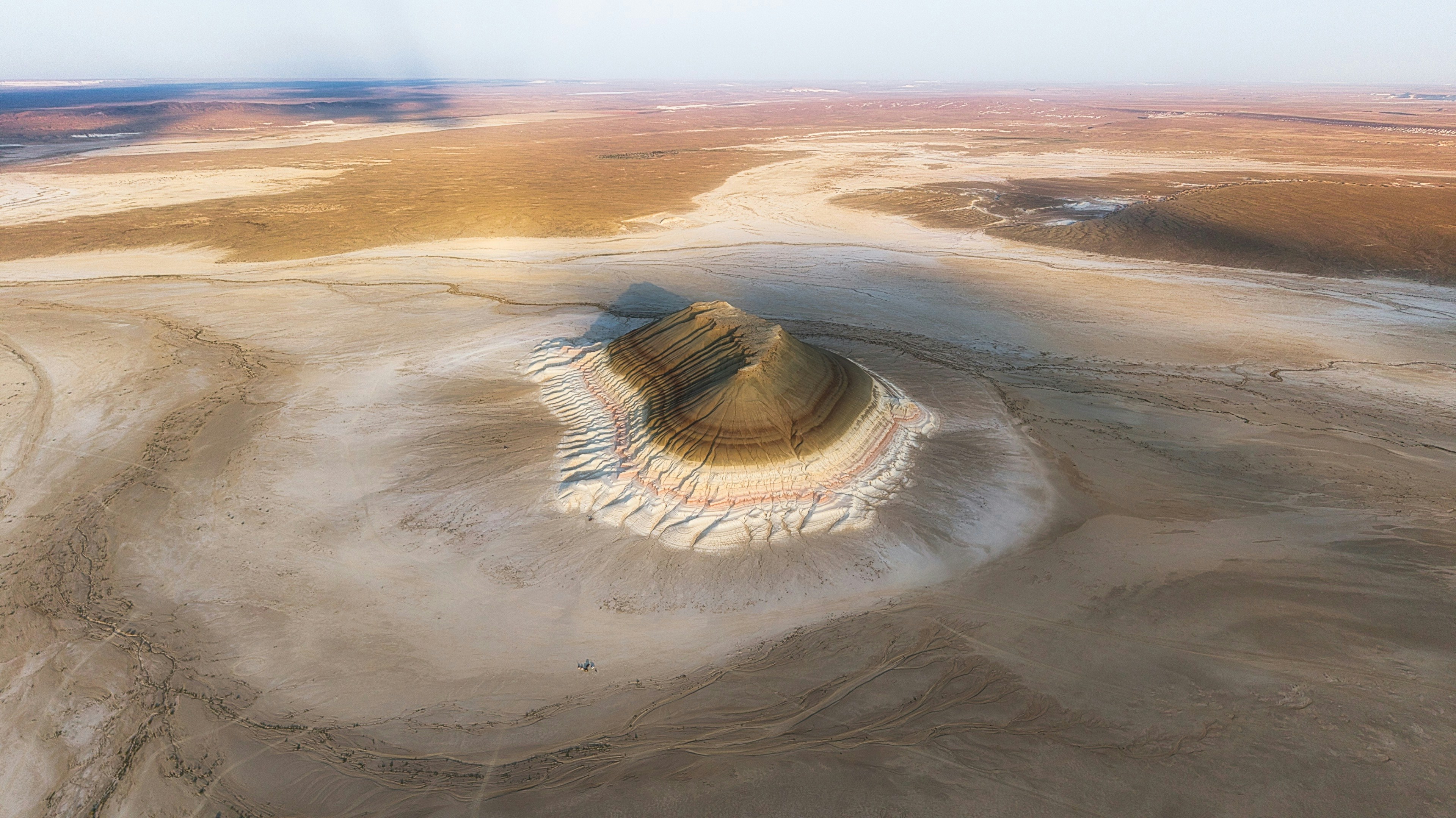 An aerial view of a solitary striped hill rising from a vast desert landscape
