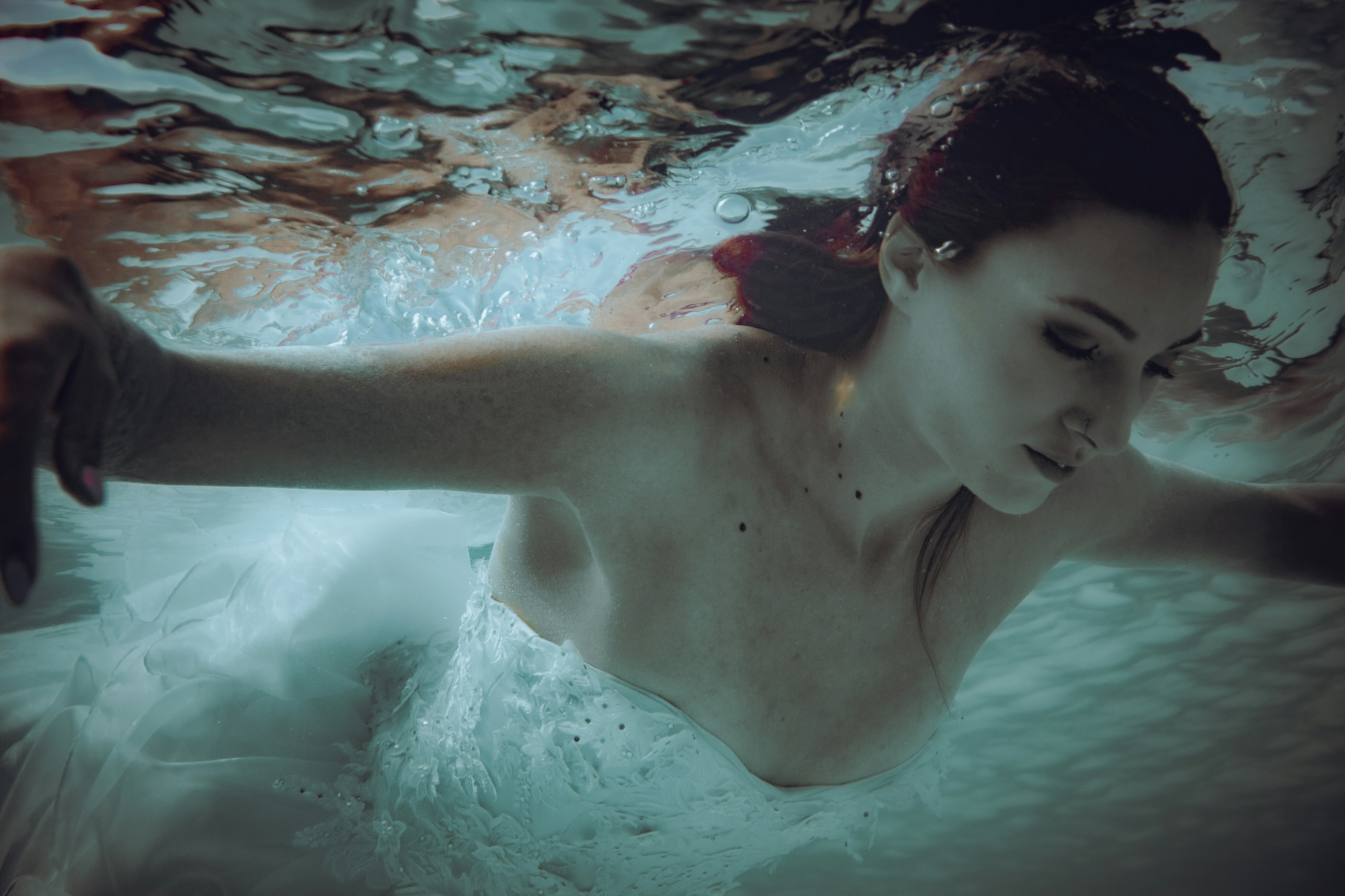 A woman in a white wedding dress swimming underwater with bubbles