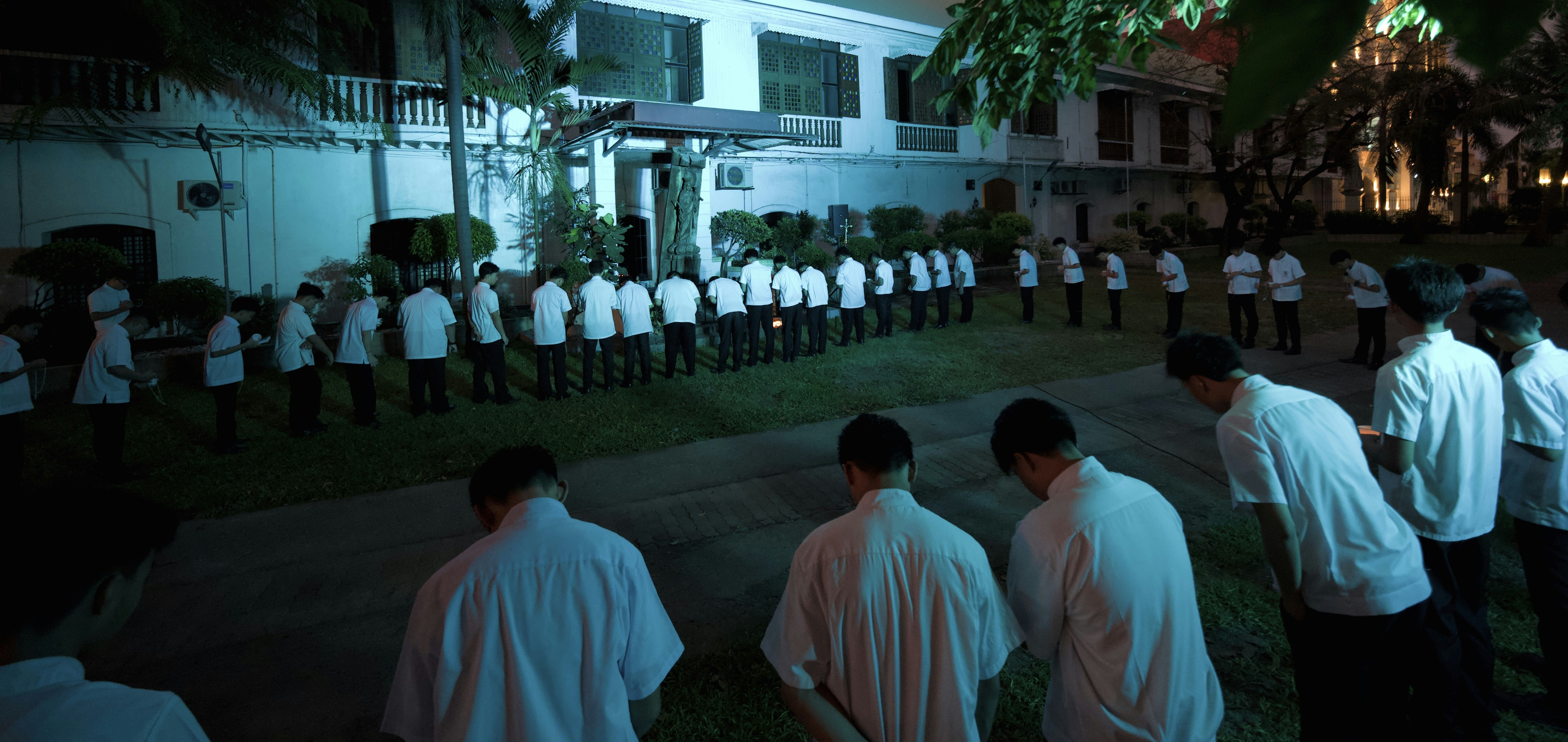 A group of people in white shirts bowing their heads in a night garden