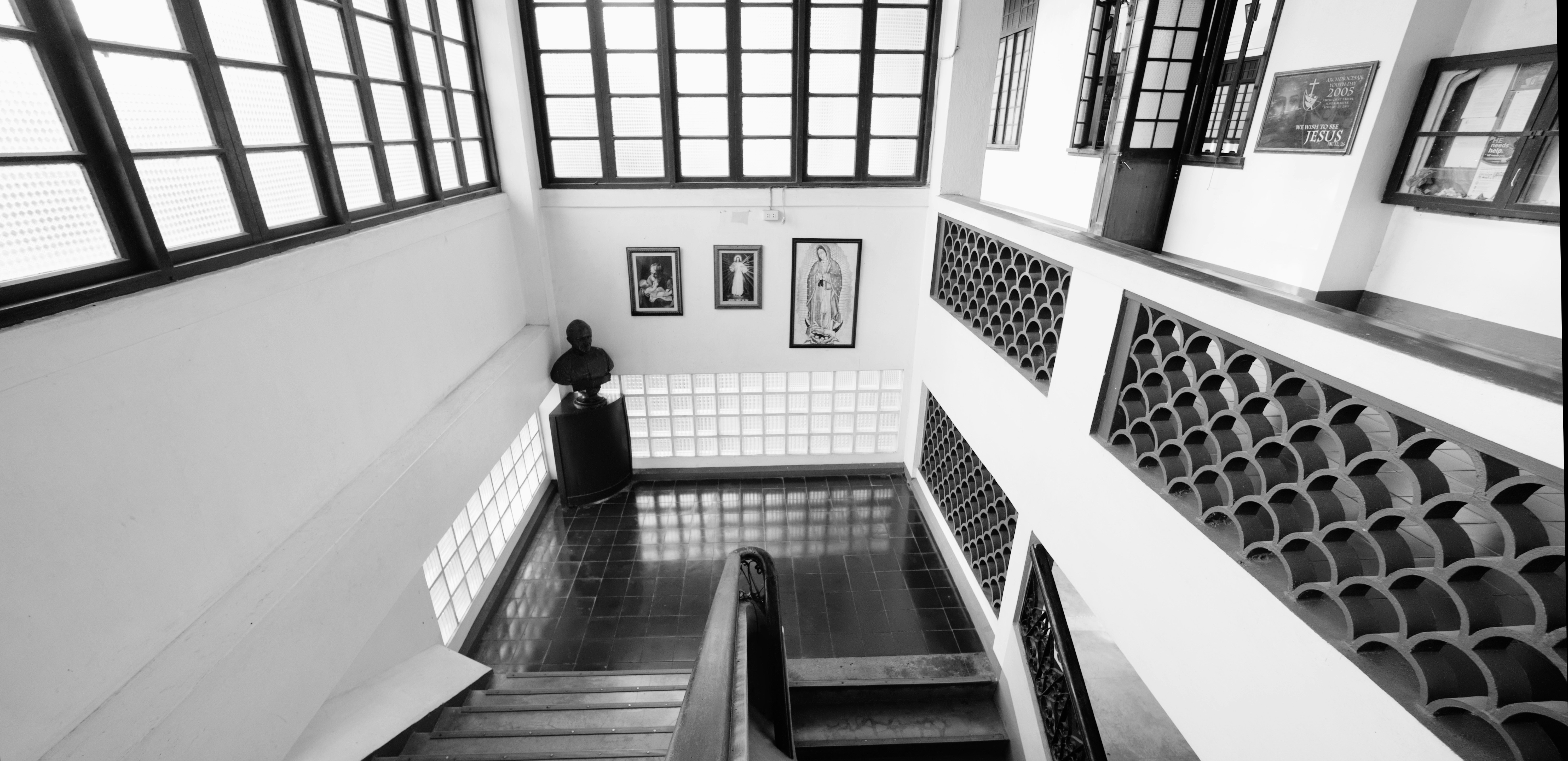 A black and white view of a staircase landing with religious art and a bust