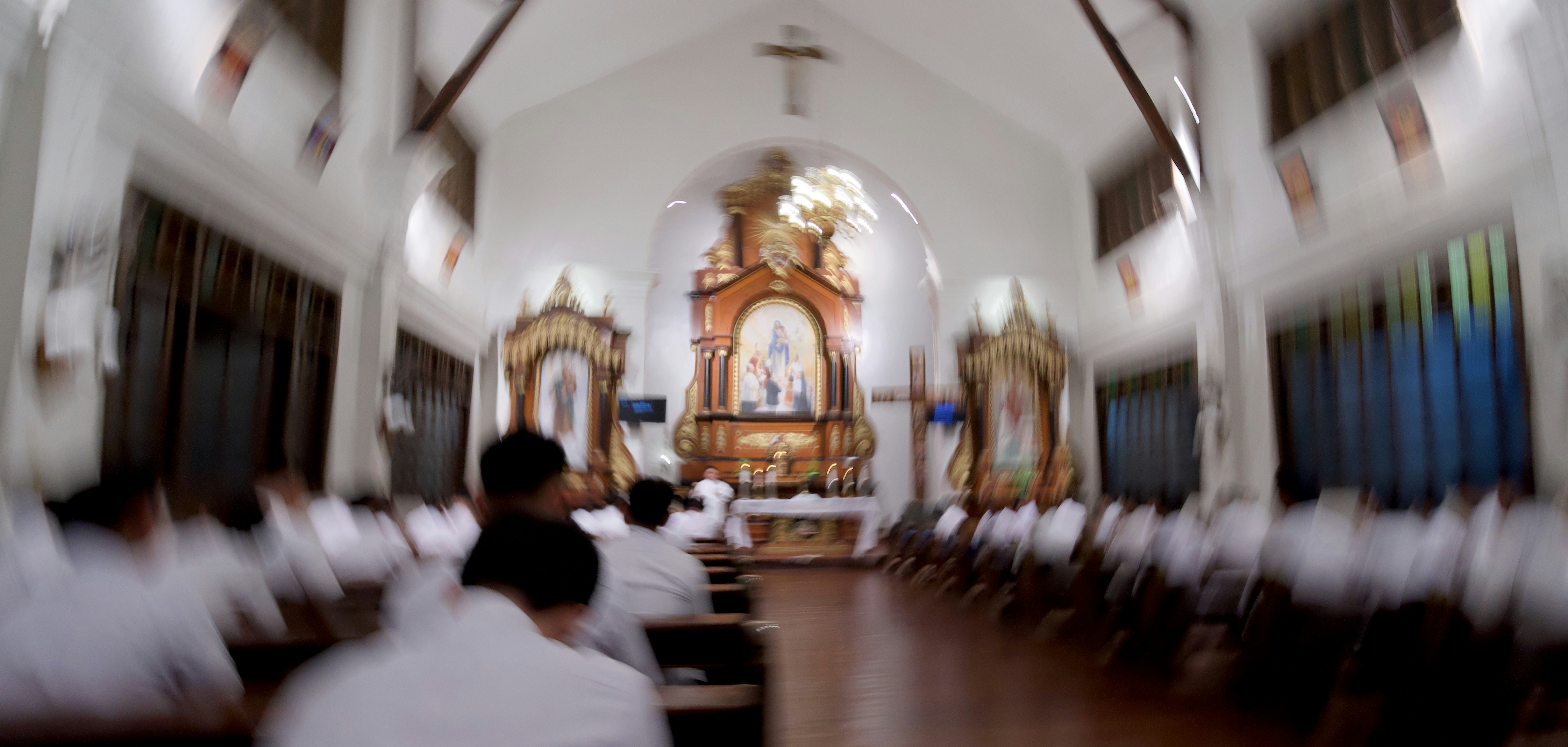 People in white shirts sitting in pews inside a church with a wooden altar