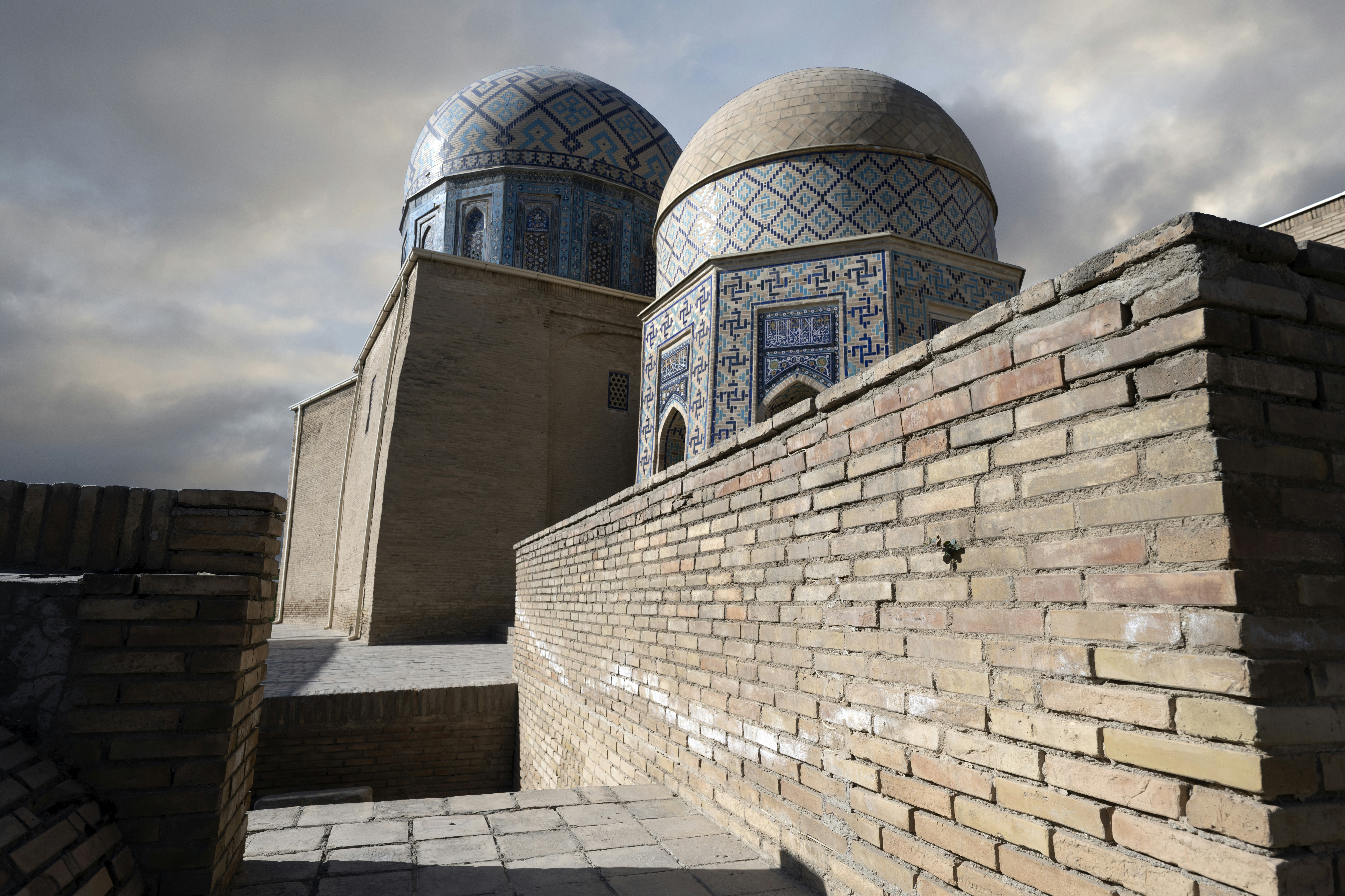 Two tiled domes of a mosque rising above a weathered brick wall