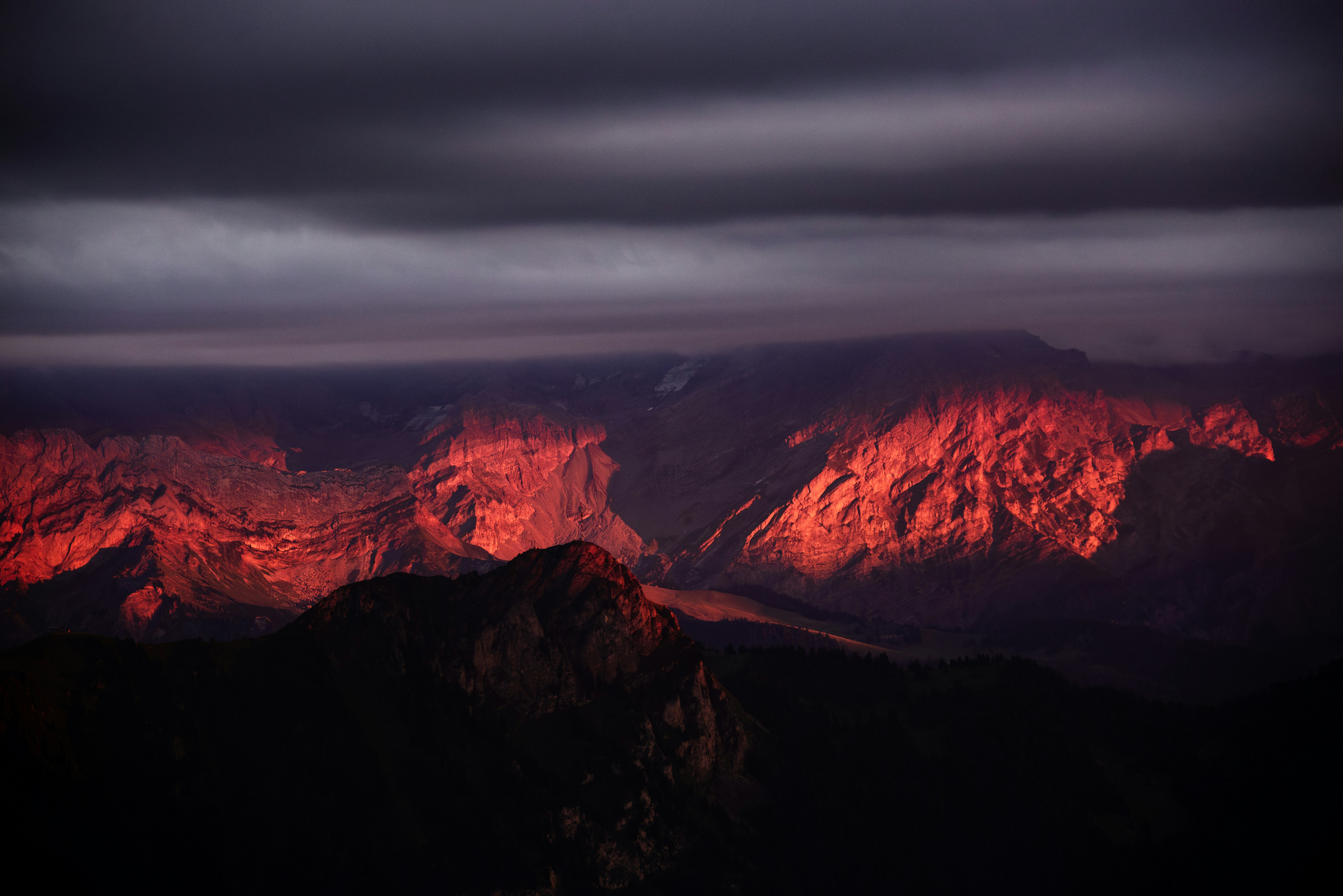 Rugged mountain peaks illuminated by warm red light under a dark cloudy sky