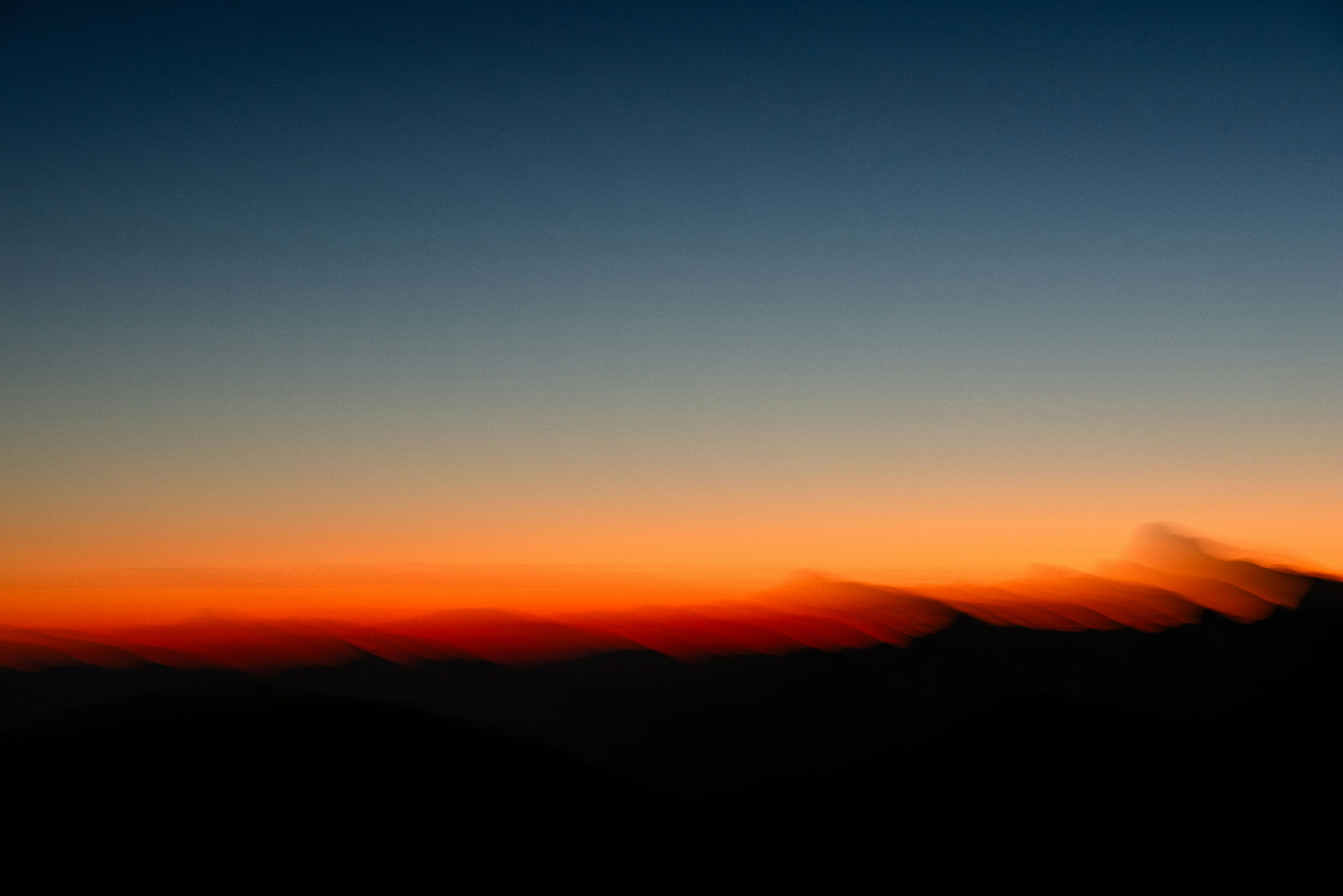 Blurred mountain silhouettes against a vibrant orange and deep blue sky